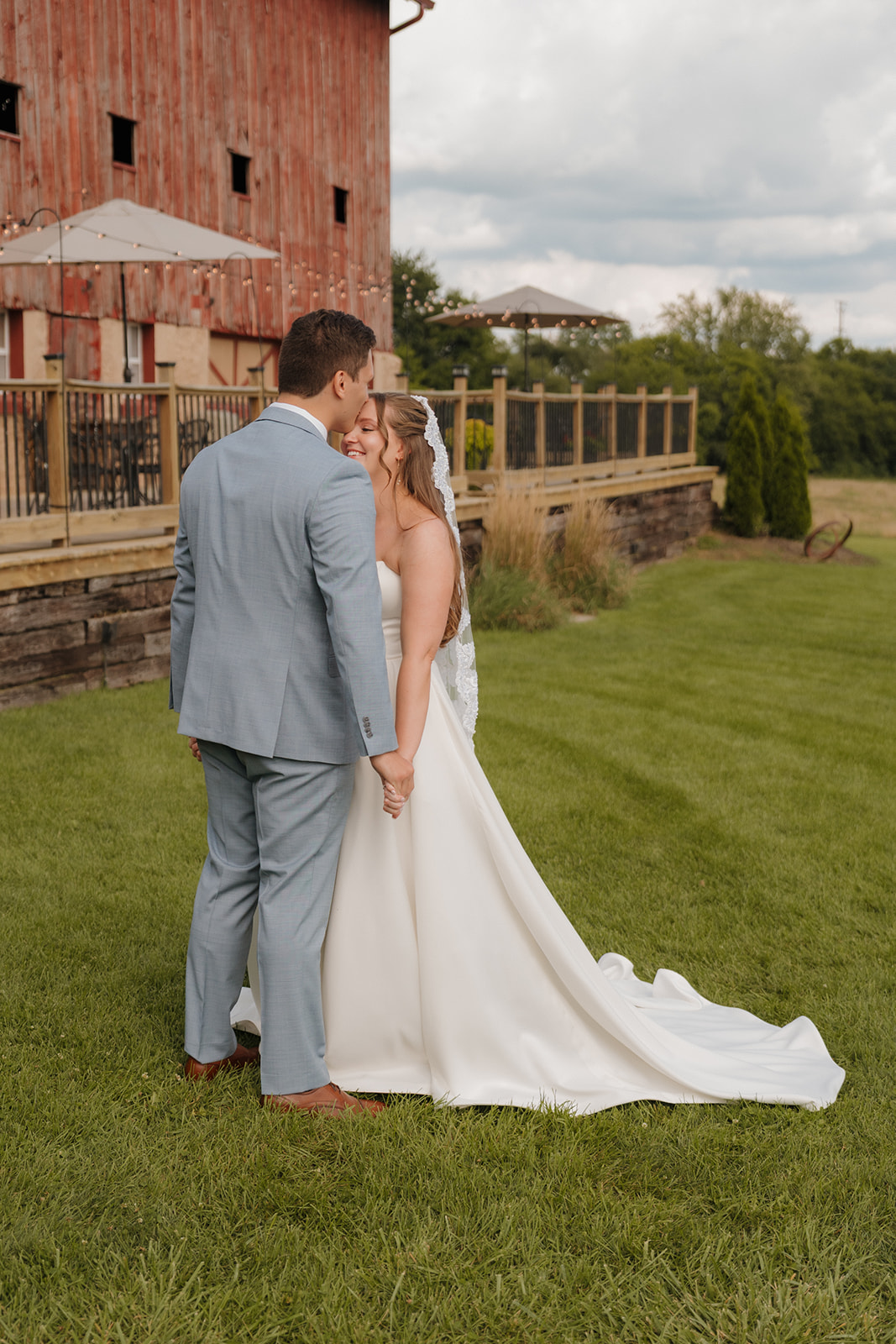 An intimate kiss between the bride and groom beside a historic red barn, surrounded by greenery and romance.
