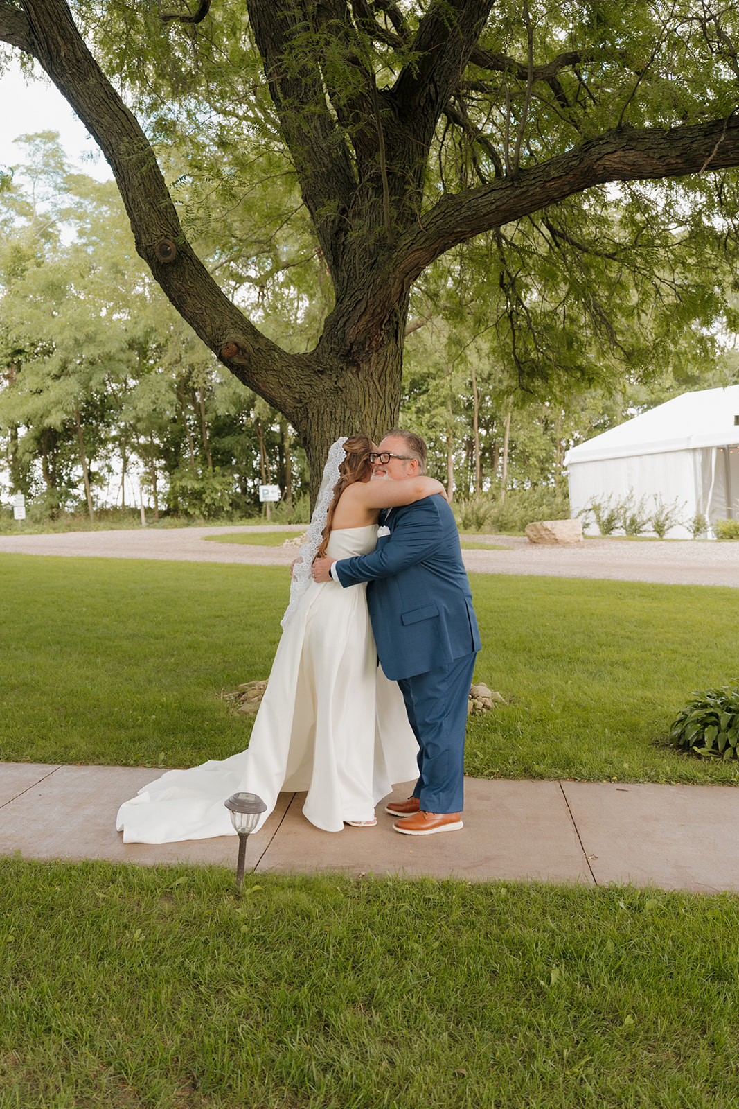 A heartfelt first look moment as the bride embraces her father beneath a shady tree on the venue’s peaceful lawn.