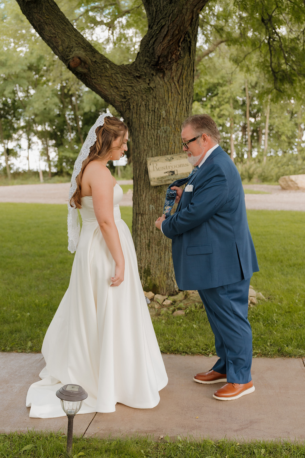 Bride and her father share a quiet, emotional moment as he presents her with a special gift beneath a tree.