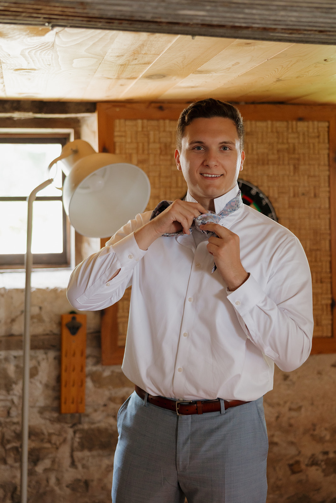Getting ready in one of the coziest spaces at a Madison wedding venue, the groom adjusts his floral bowtie in warm morning light.