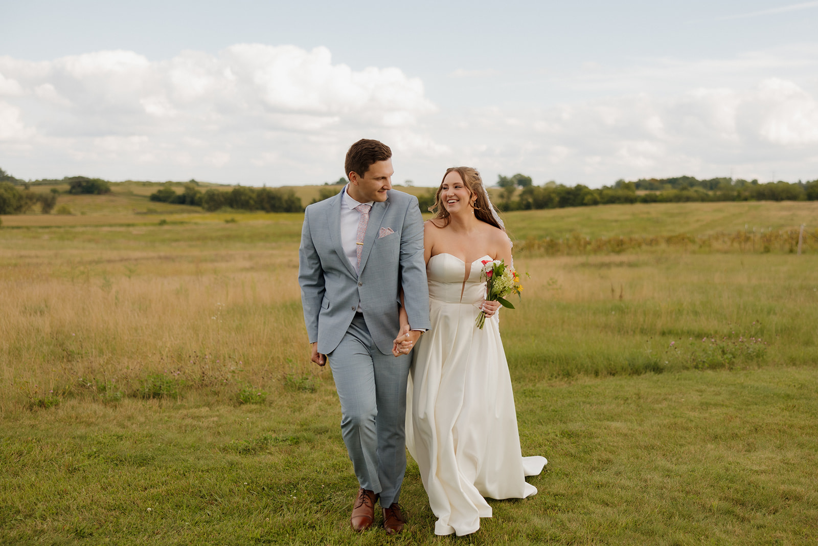 Just married joy: bride and groom walking hand-in-hand through golden grass at one of the dreamiest Madison wedding venues.