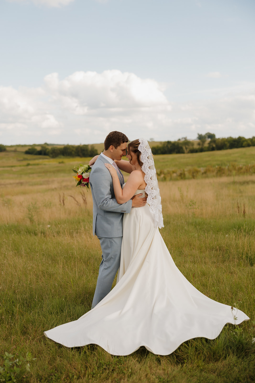 A romantic meadow kiss framed by a flowing veil and train—another reason Madison wedding venues feel like magic.
