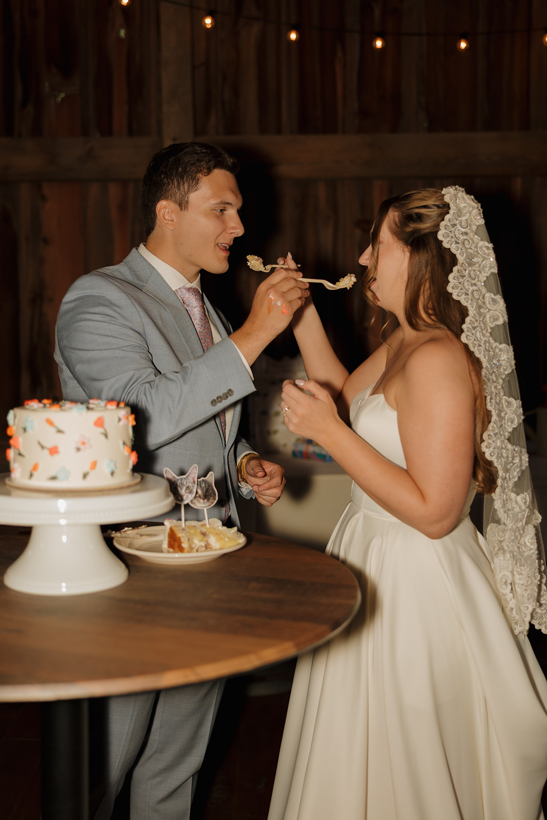 Classic cake-cutting moment as the groom sweetly feeds the bride their floral-adorned mini cake.