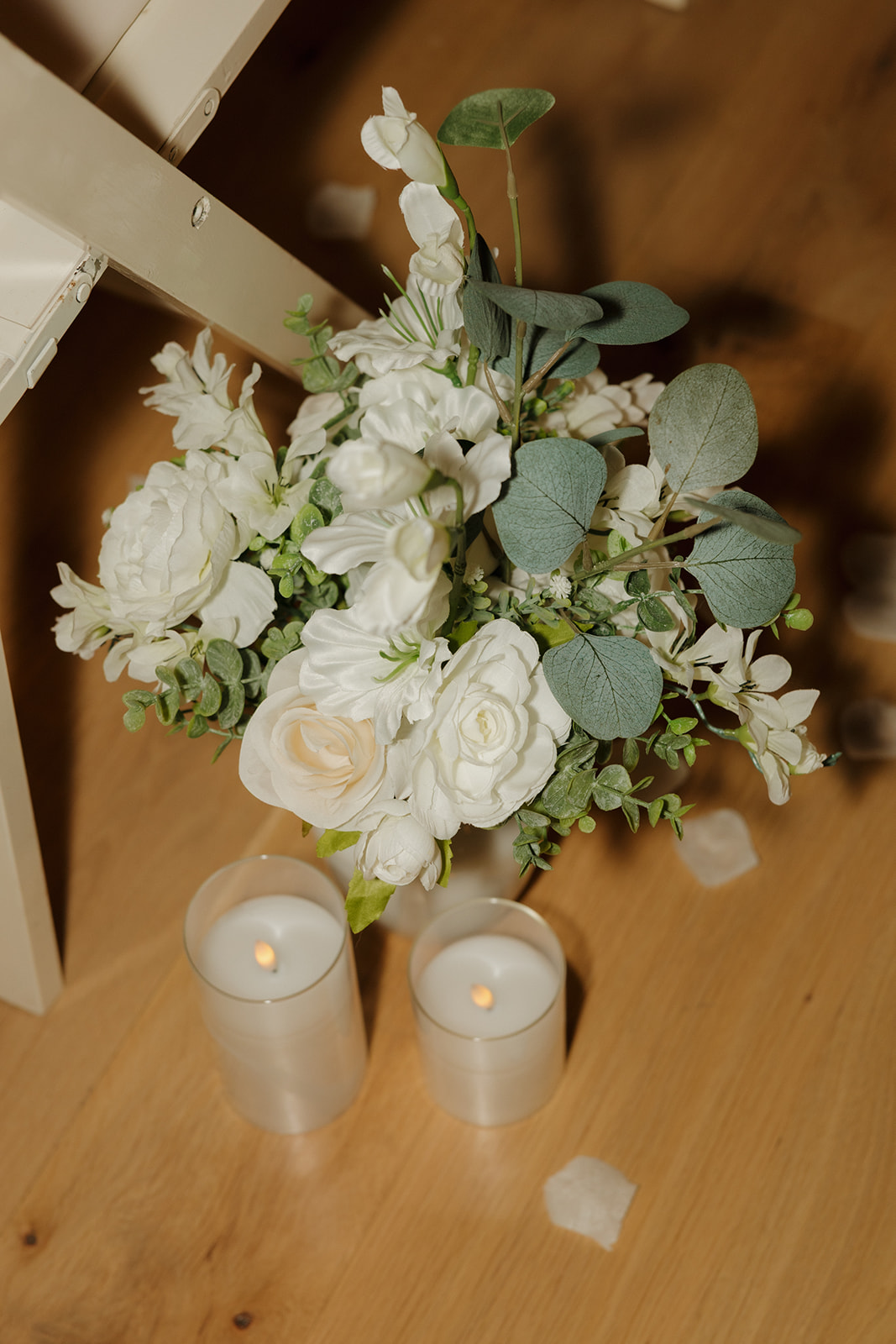 White roses, eucalyptus, and lush greenery sit at the end of an aisle row, paired with glass candleholders for a simple and elegant touch.