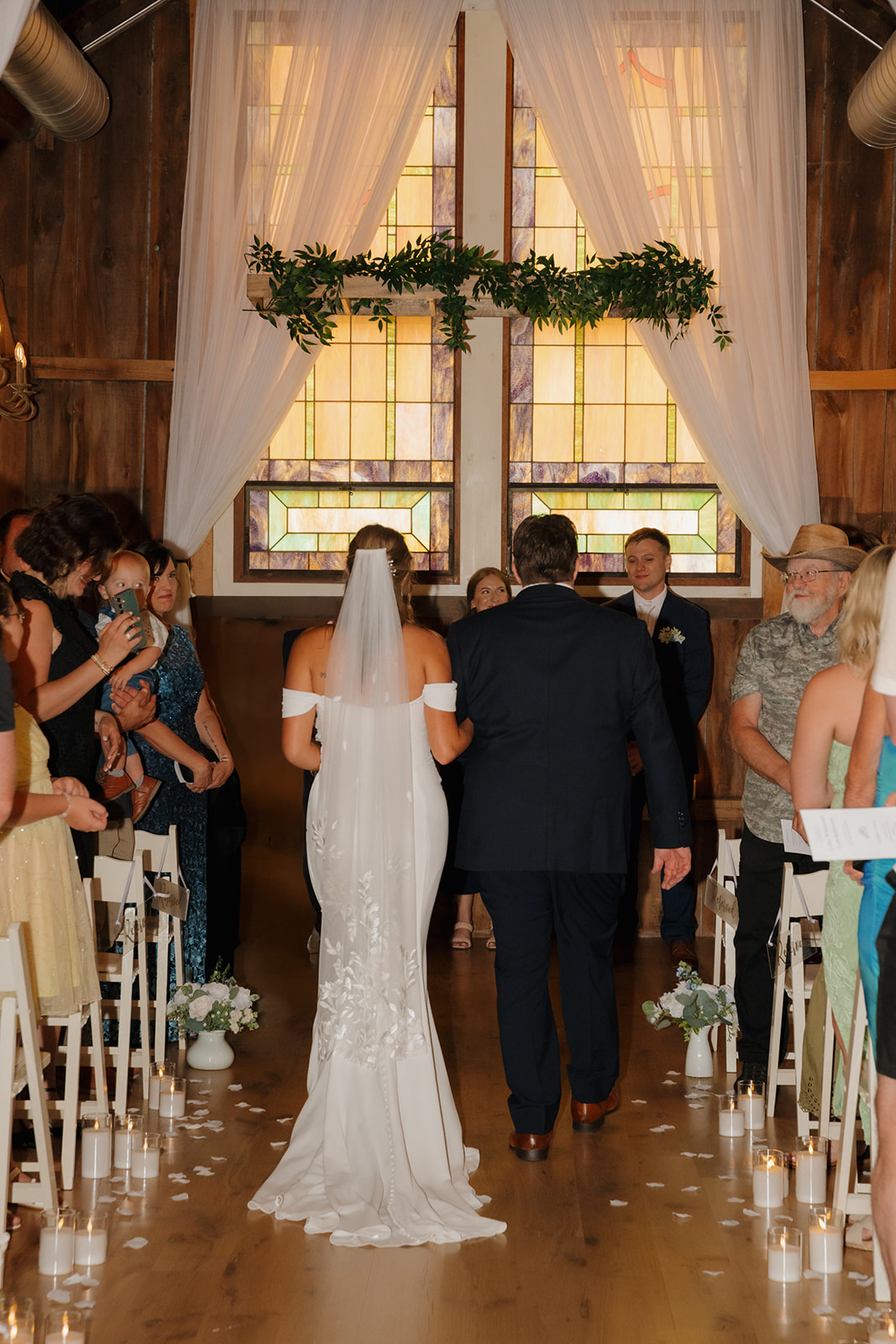 The bride walks arm-in-arm with her father down a candlelit aisle in a warm, wood-paneled barn—an emotional moment beautifully captured by a wedding photographer in Wisconsin.