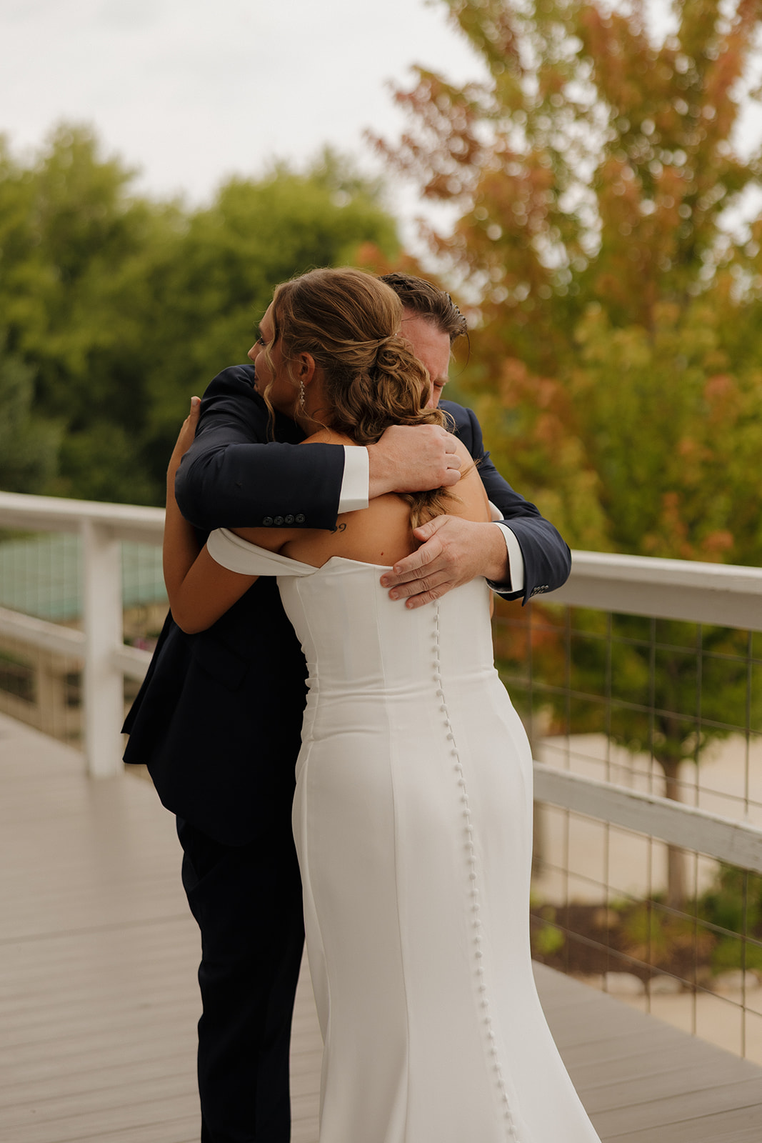 The bride and her father share a heartfelt embrace on a deck overlooking autumn-colored trees—an emotional first look moment.