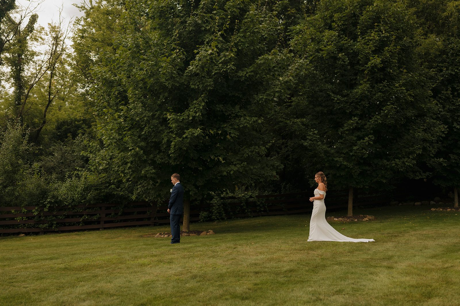 The bride walks slowly toward her groom for their first look, surrounded by tall trees and golden hour light—an intimate moment beautifully captured by a wedding photographer in Wisconsin.