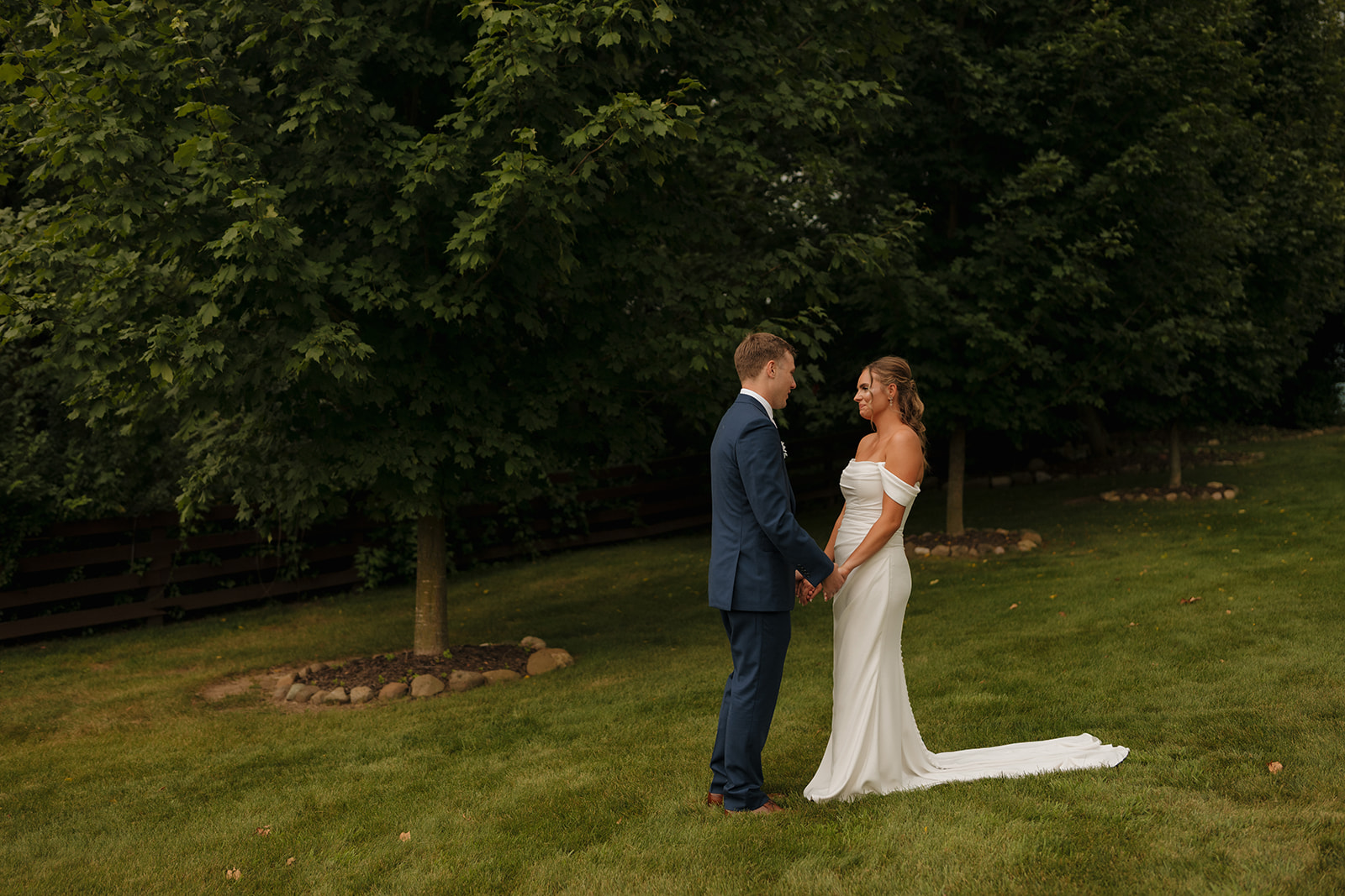 The couple shares a sweet first look, holding hands and smiling at each other under a canopy of trees—captured by a wedding photographer in Wisconsin.