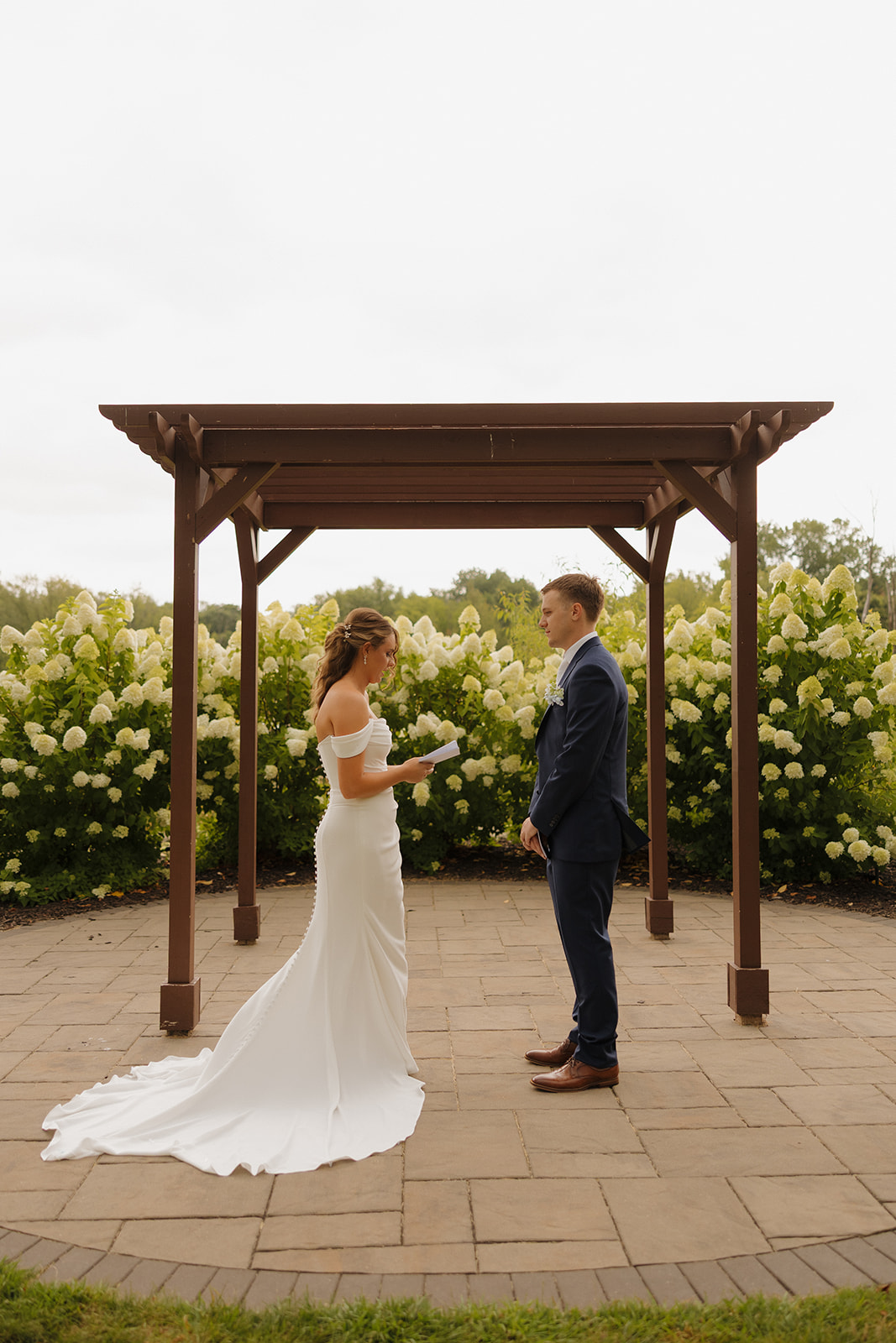 A bride stands in front of her groom, reading personal vows in a white gown with buttons down the back—an emotional moment photographed by a wedding photographer in Wisconsin.