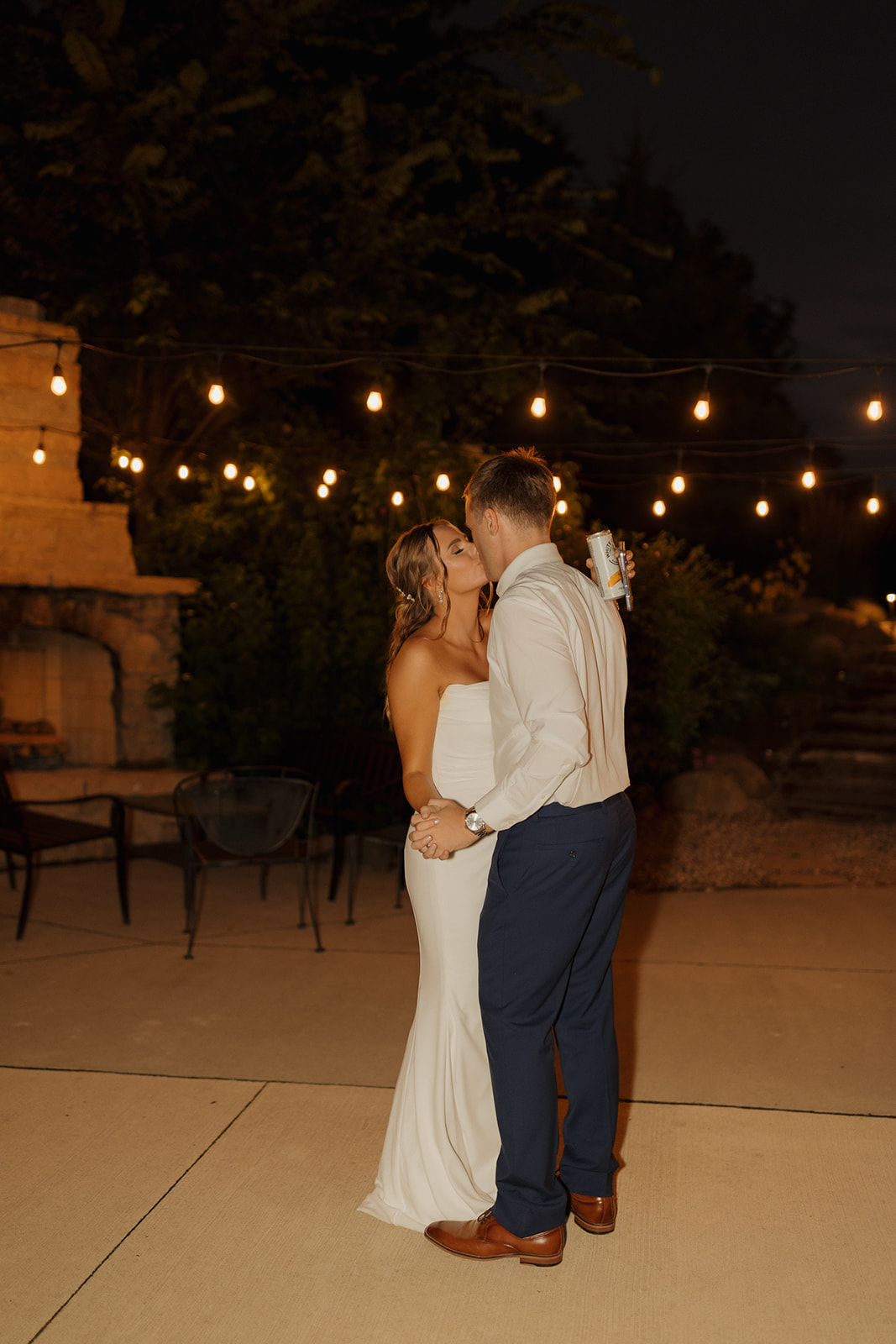 Newlyweds share a romantic kiss during their first dance, with soft string lights illuminating the night—a cozy, candid scene photographed by a wedding photographer in Wisconsin.