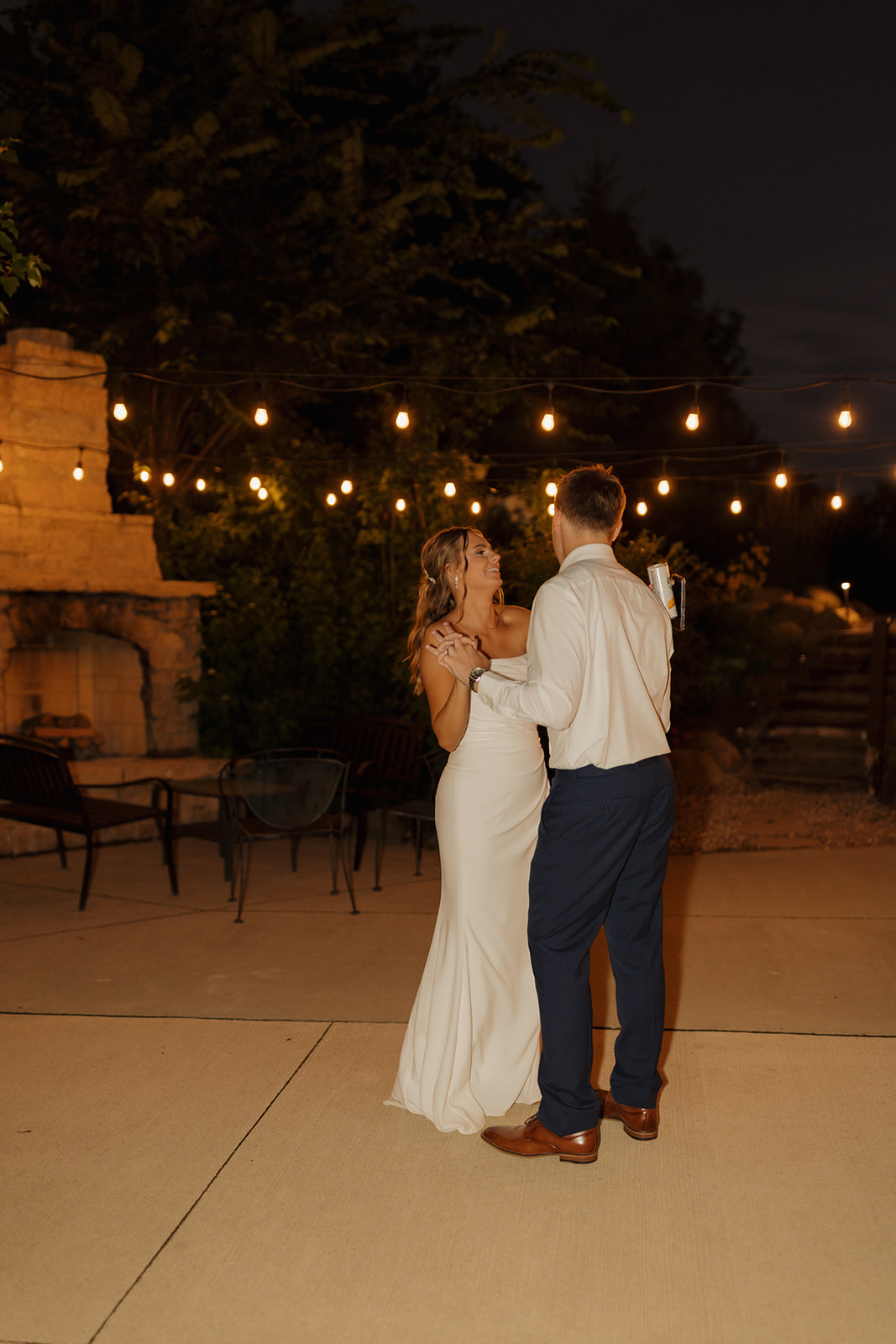 A bride and groom share a joyful first dance beneath glowing string lights on a patio, creating a dreamy nighttime moment captured by a wedding photographer in Wisconsin.