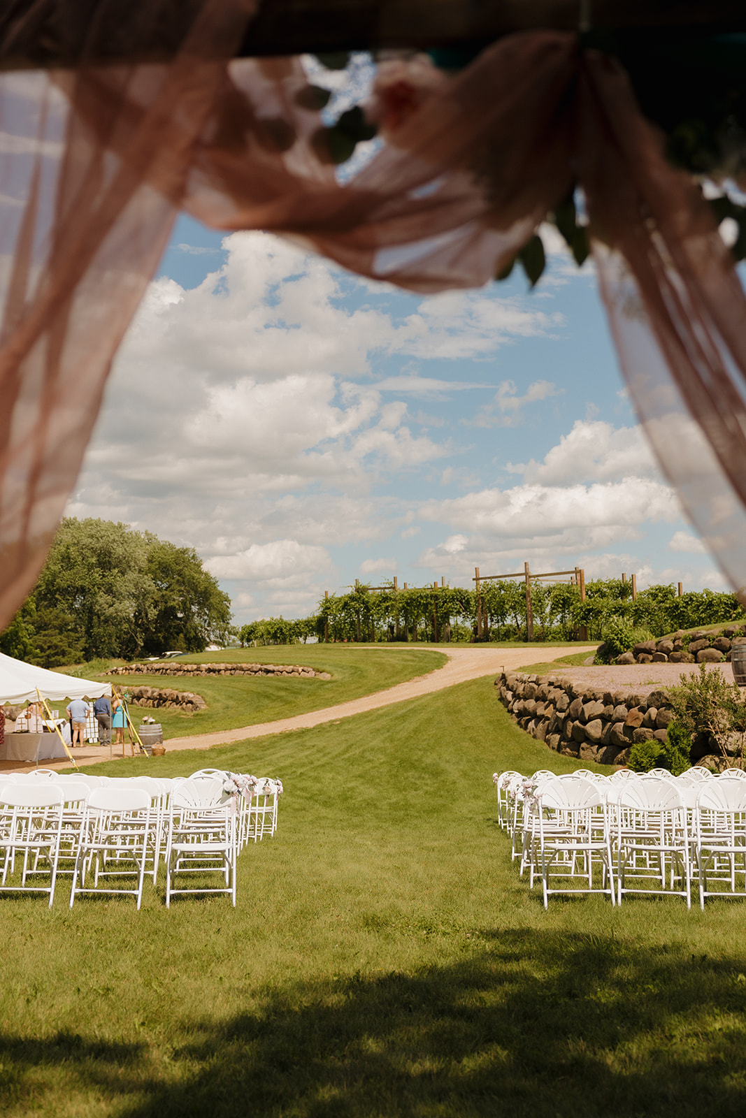 Scenic vineyard path seen through pink draping on the ceremony arch at a Wisconsin wedding venue.