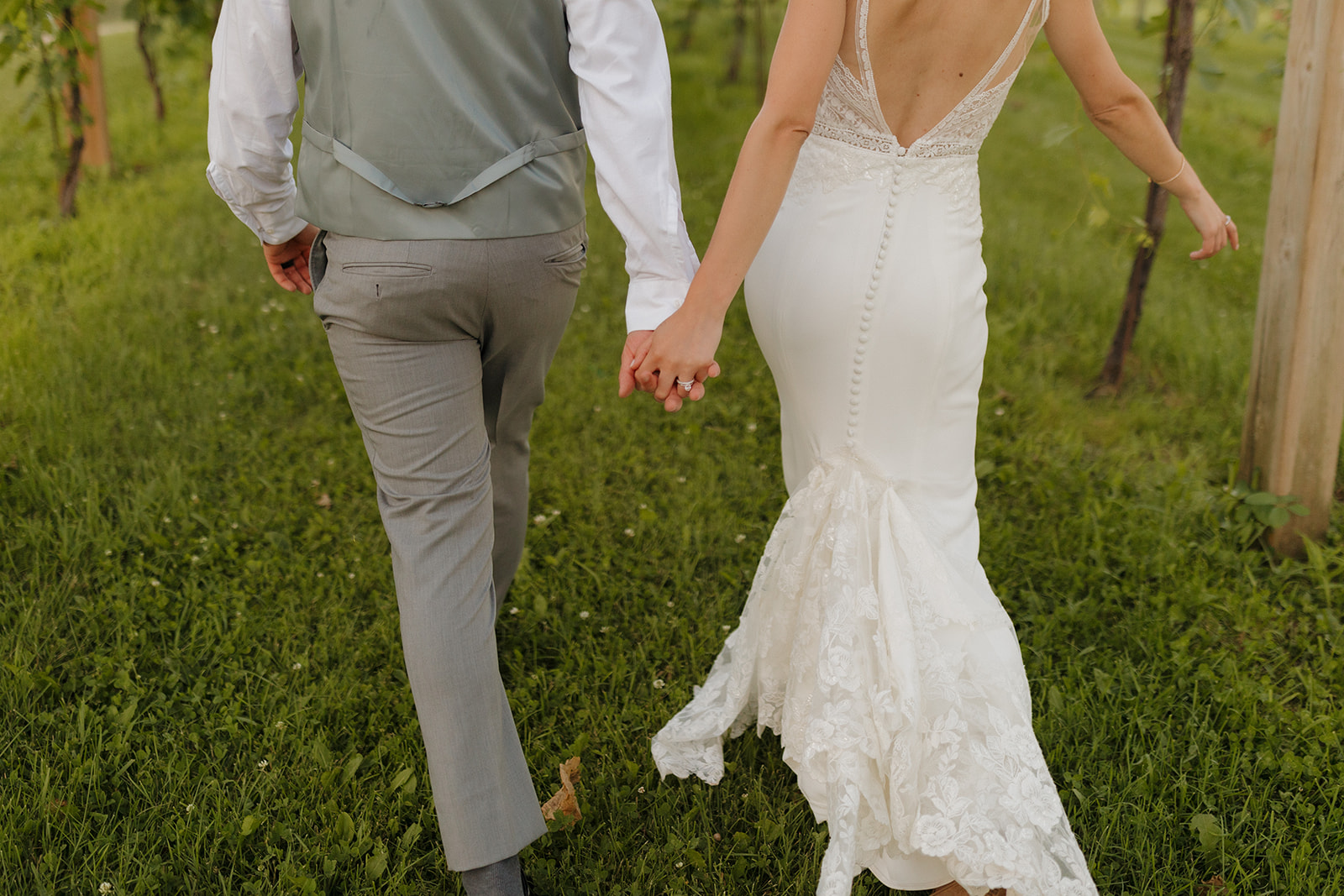 Bride and groom walk hand-in-hand through vineyard rows at a Wisconsin winery wedding venue.