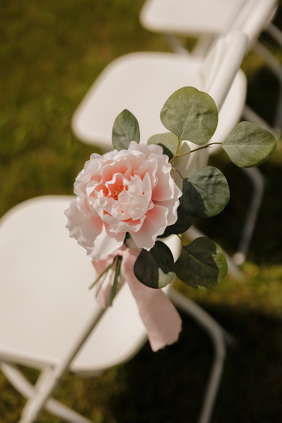 Delicate faux peony and eucalyptus stem adds charm to a ceremony chair.