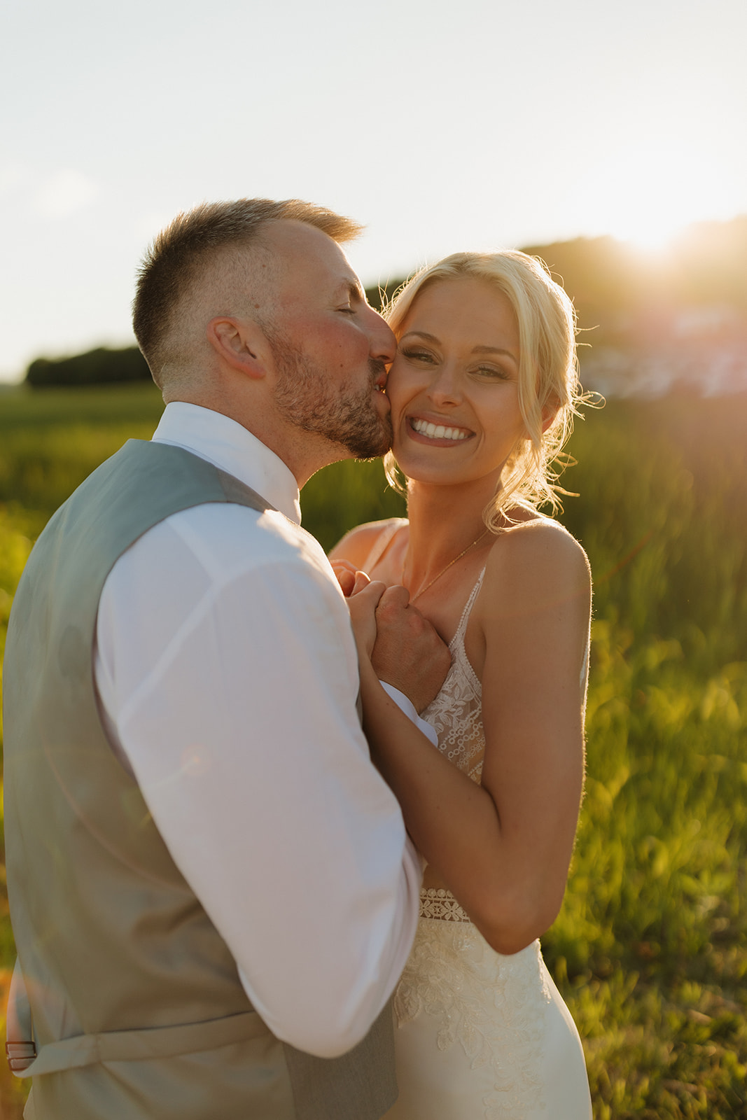 Bride smiling as groom kisses her cheek during golden hour portraits at a Wisconsin wedding venue.