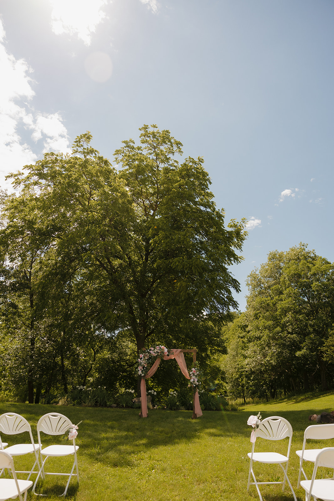 Ceremony setup under a shady tree with pink florals and fabric at a Wisconsin wedding venue.