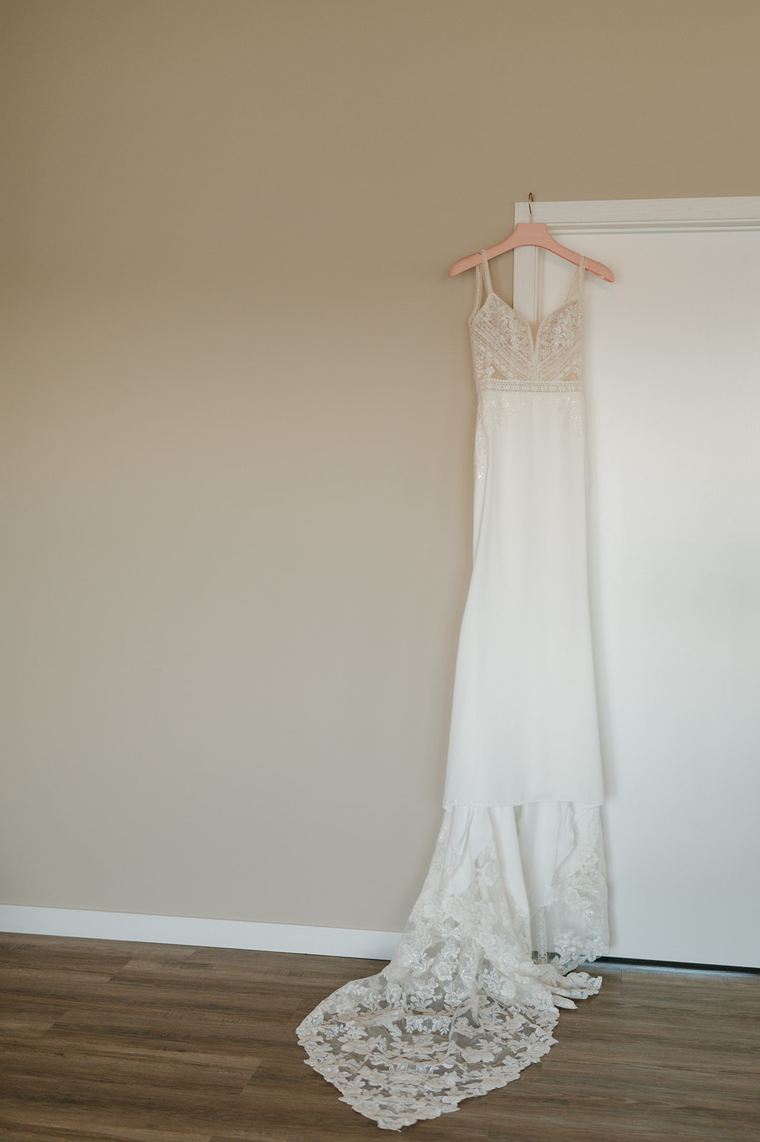 Elegant lace wedding gown hanging against a neutral wall before a vineyard wedding in Wisconsin.