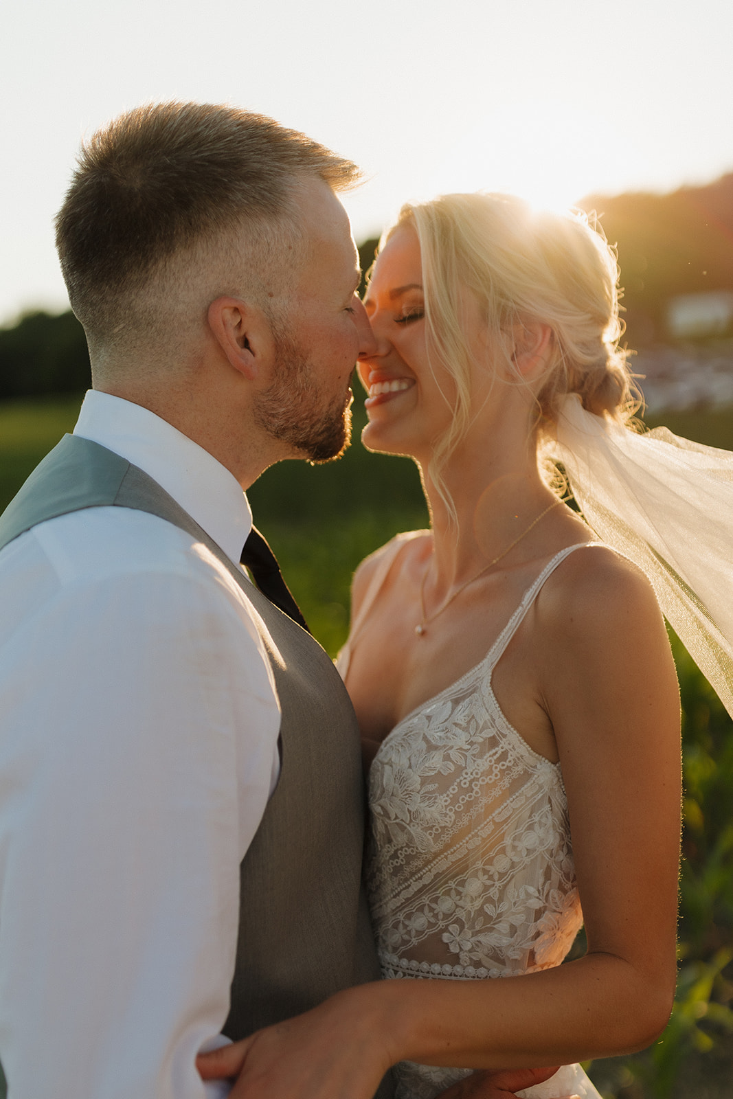 Bride and groom embrace in the middle of a golden field at sunset.