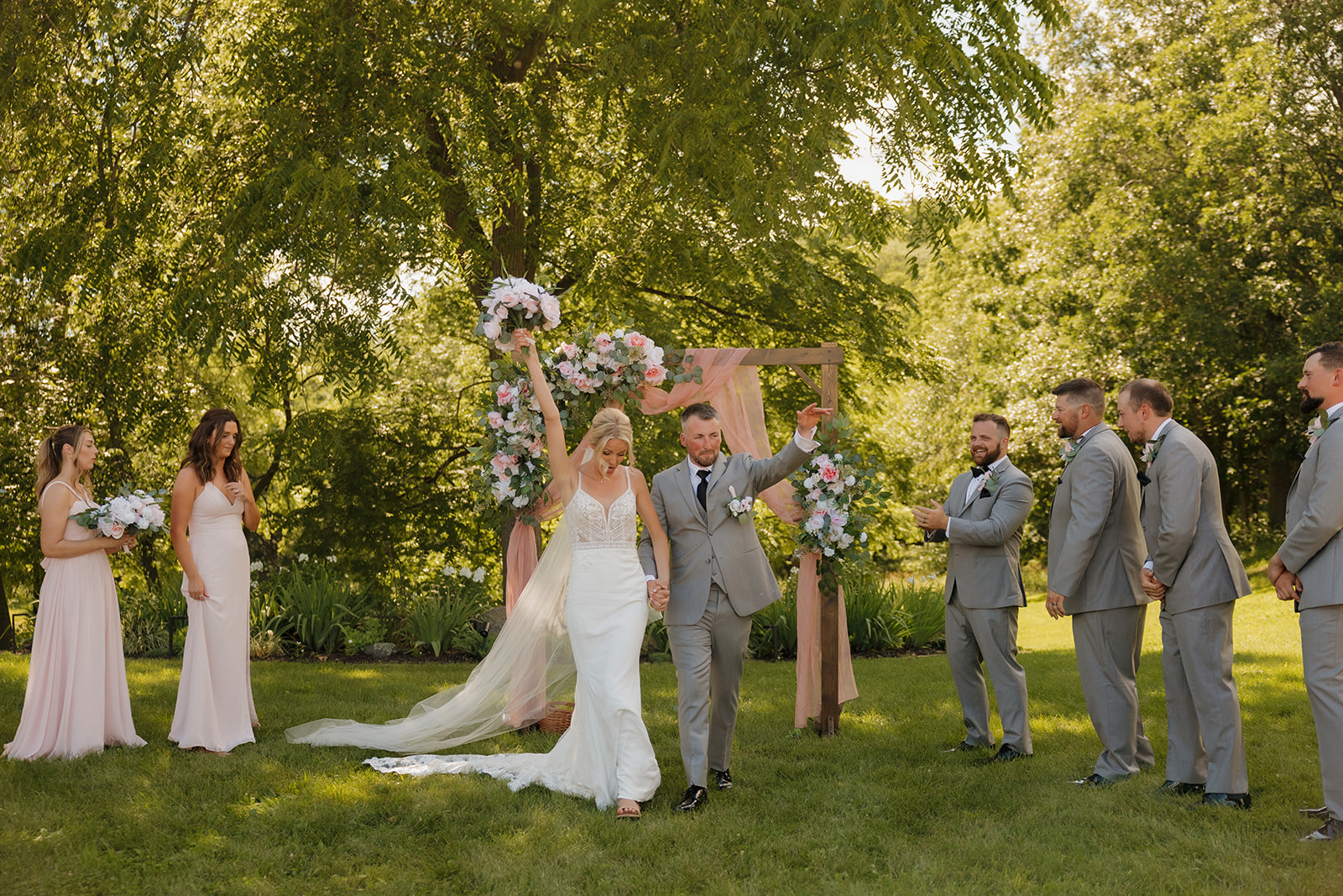 Just married! Couple raises hands in celebration at their vineyard wedding ceremony.