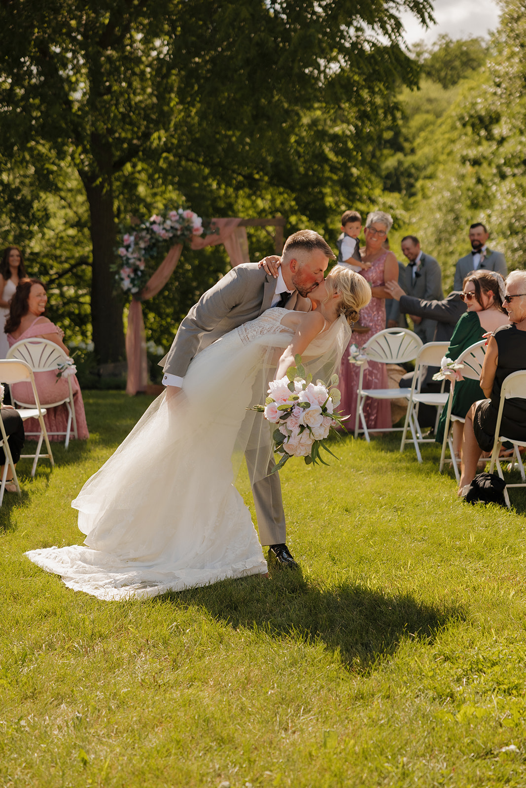 Groom dips his bride for a joyful kiss as guests cheer at a Wisconsin winery wedding.