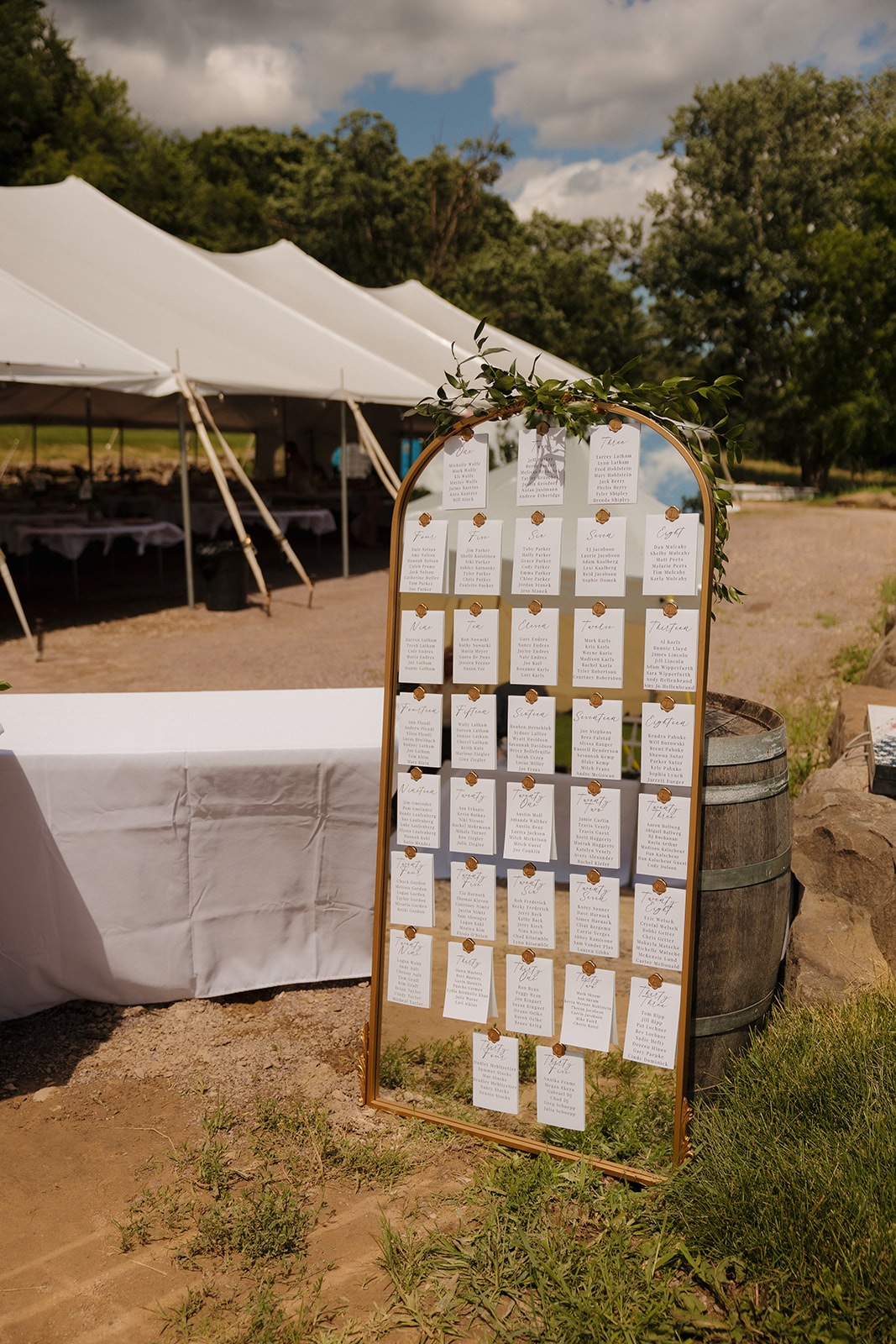 Mirror seating chart display with handwritten name cards and greenery accents.