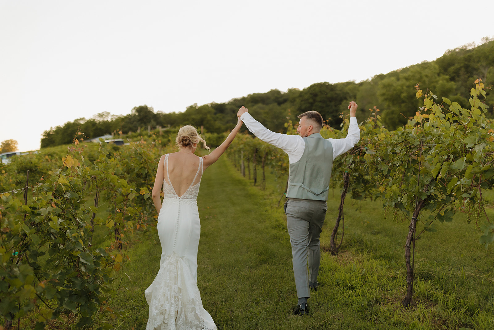 Bride and groom celebrating hand-in-hand while walking through vineyard at sunset in a Wisconsin wedding venue.
