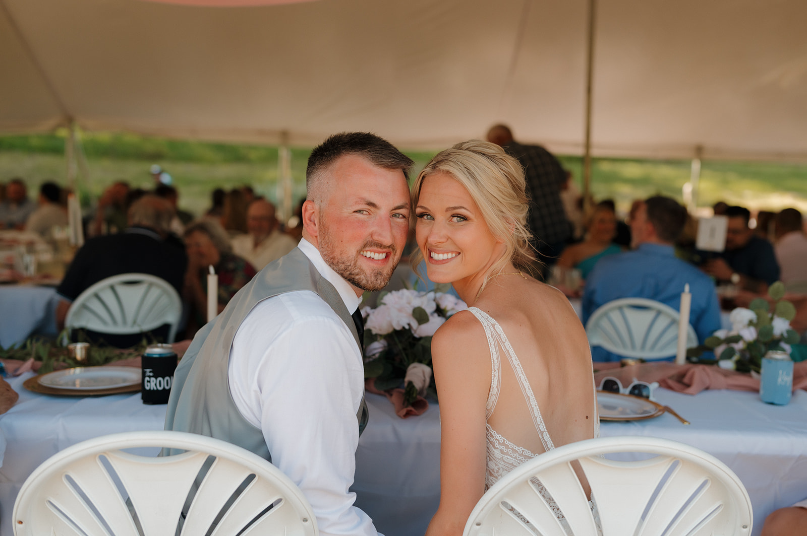 Bride and groom smile back at the camera while seated at the head table at their Wisconsin winery wedding venue.