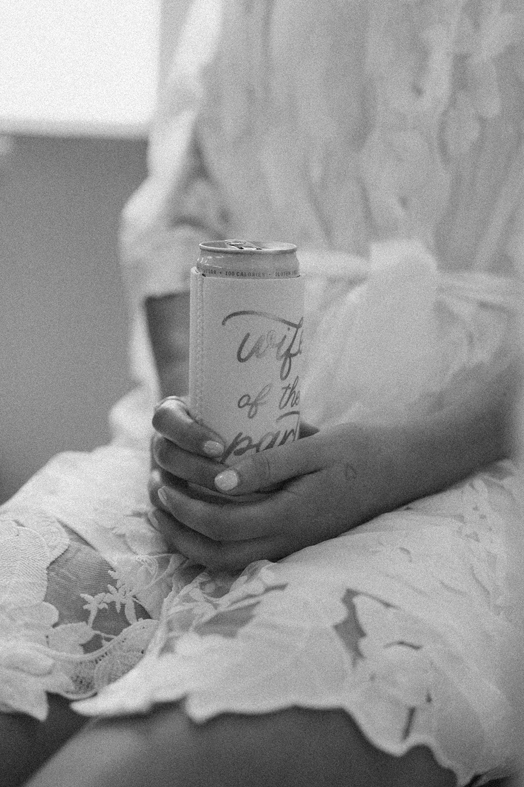Bride in lace robe holding a can with “wife of the party” koozie during morning wedding prep.