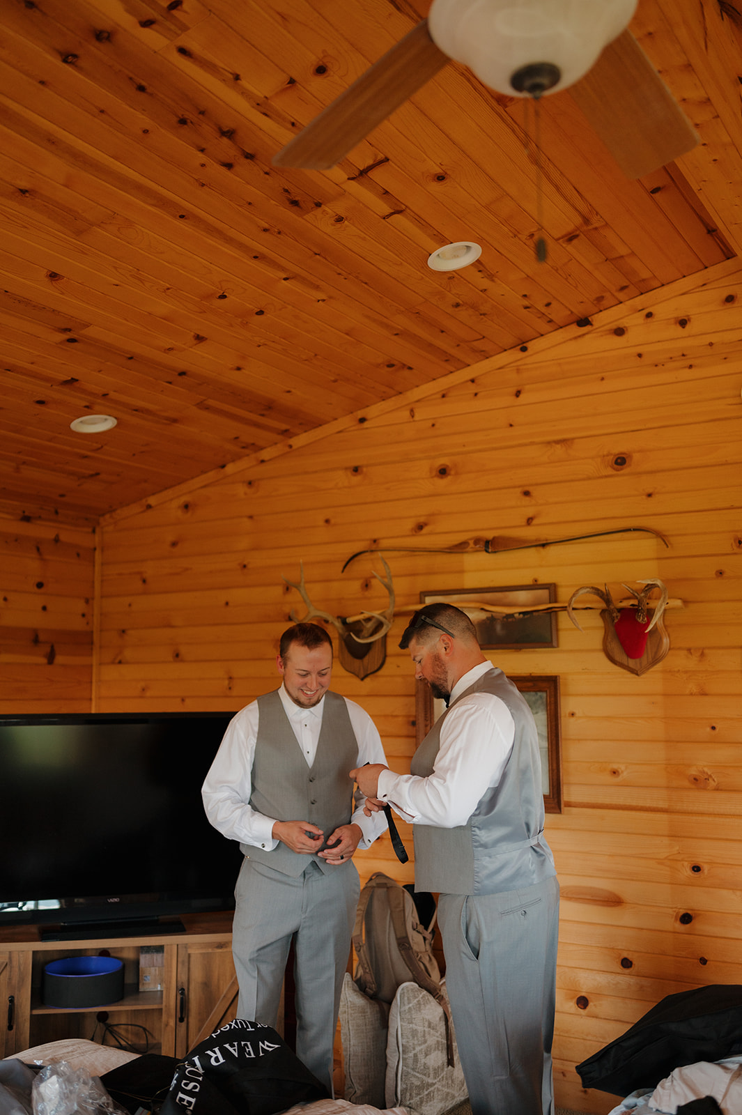 Groom shares a light moment with a groomsman while getting dressed for the wedding day.