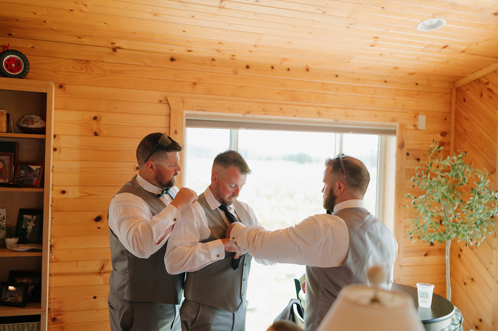 Groomsmen helping each other get suited up for the big day at a cozy cabin near a Wisconsin winery wedding venue.
