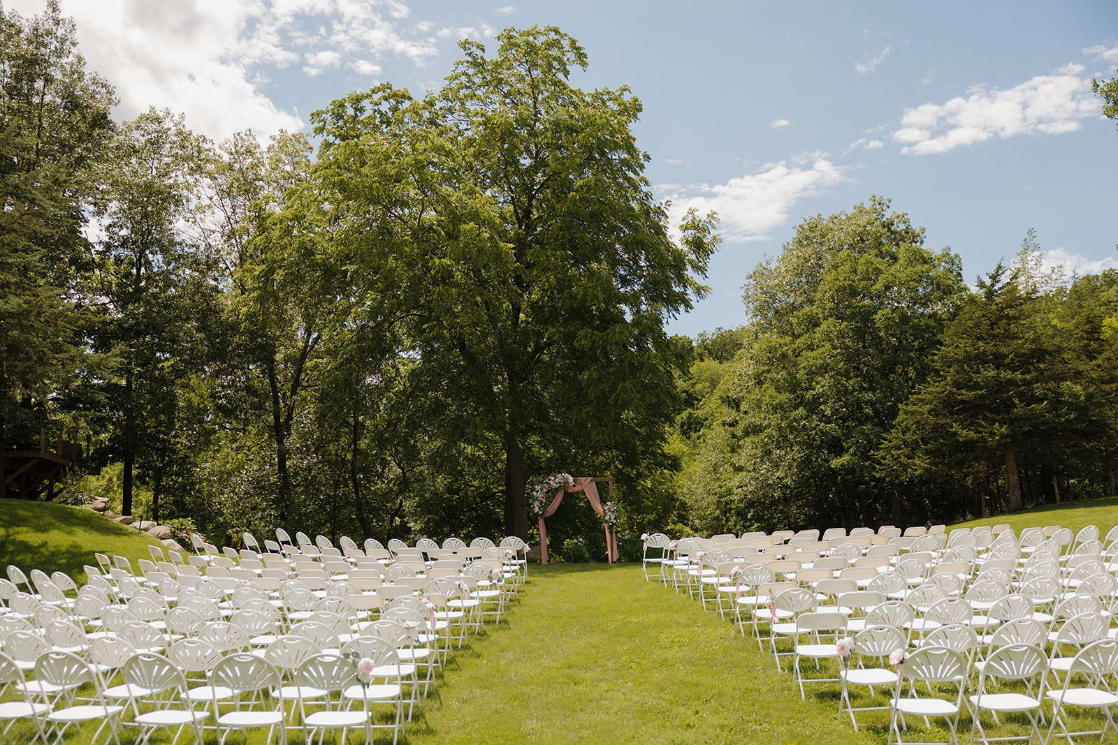 Full ceremony setup with white chairs and a floral arbor in a lush Wisconsin winery wedding venue.