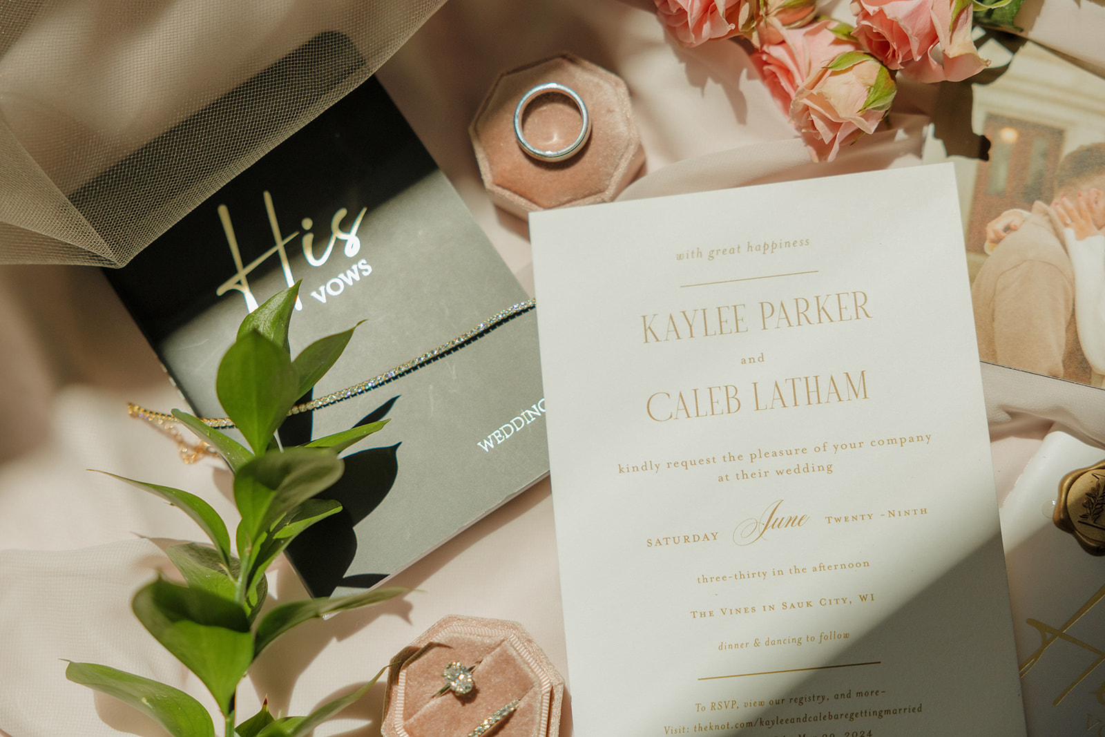 Wedding flatlay with invitation, ring box, and vow books styled with pink roses and soft light.