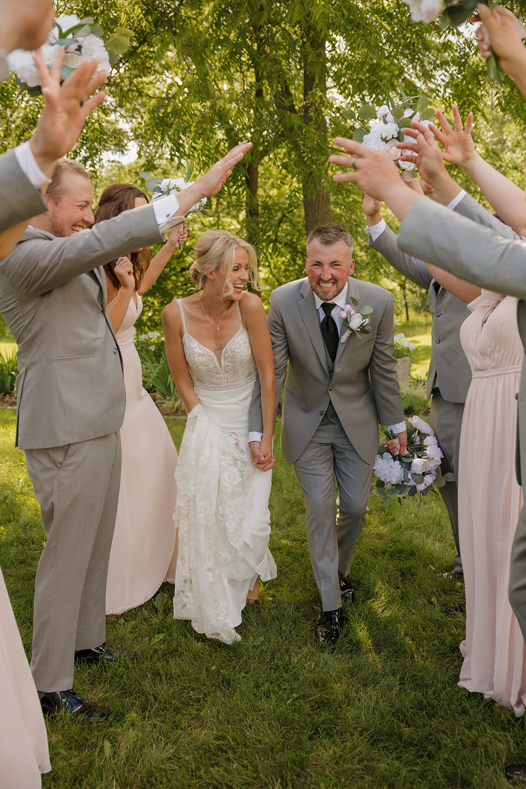 Bride and groom laugh as their wedding party cheers and creates an arch with their arms.