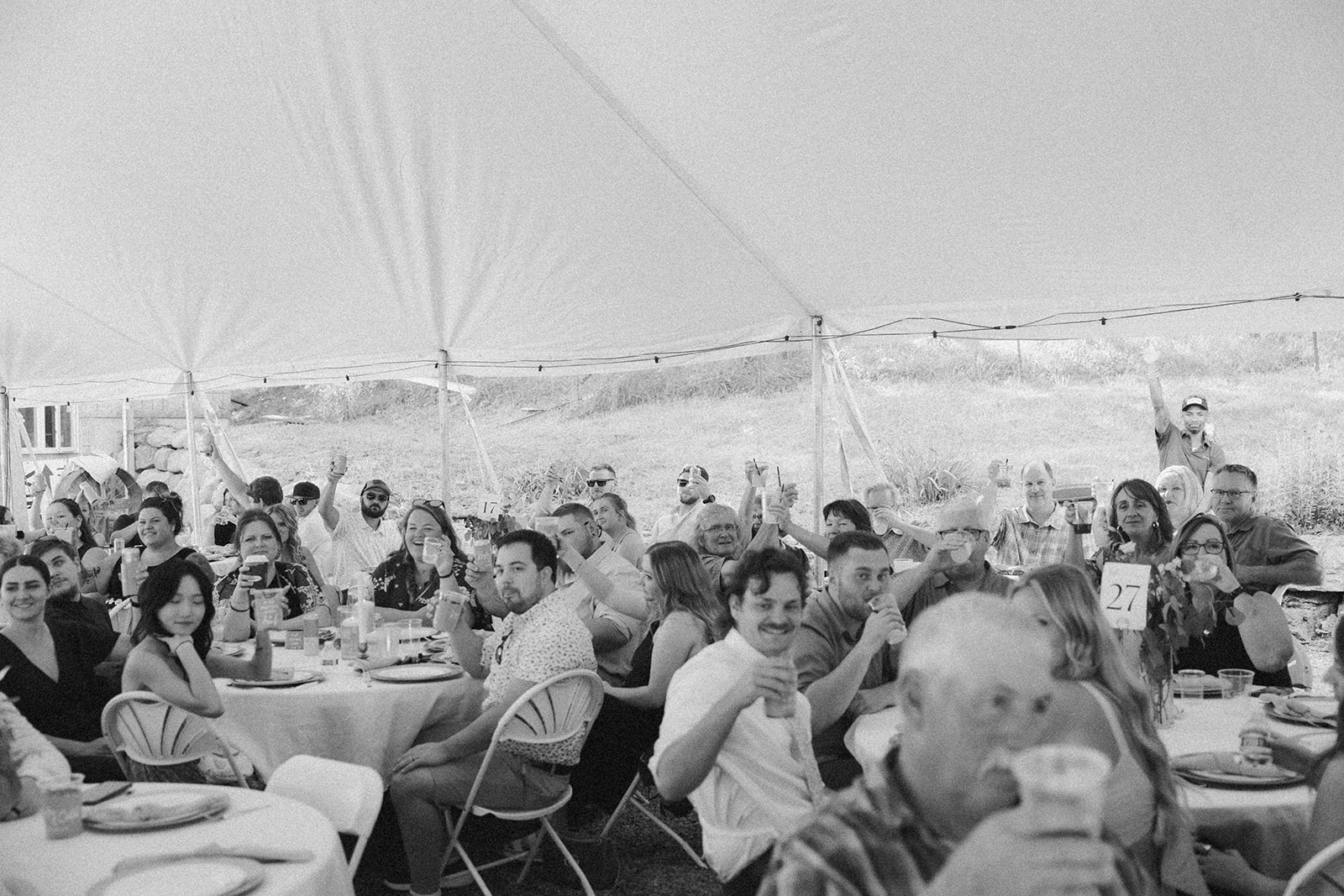 Black and white photo of guests raising drinks and cheering during the reception.