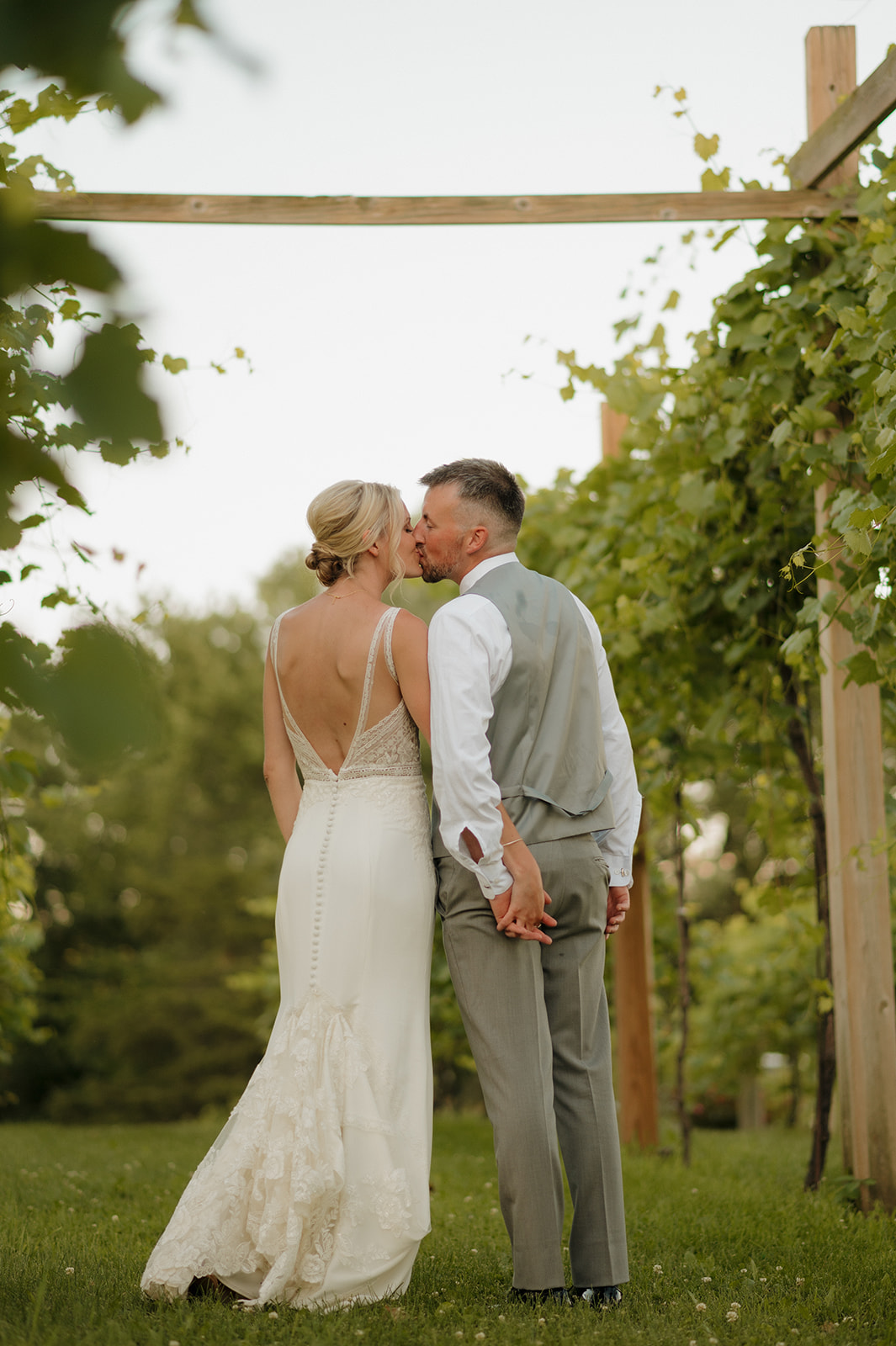 Bride and groom share a kiss between vineyard rows at a romantic Wisconsin wedding venue.