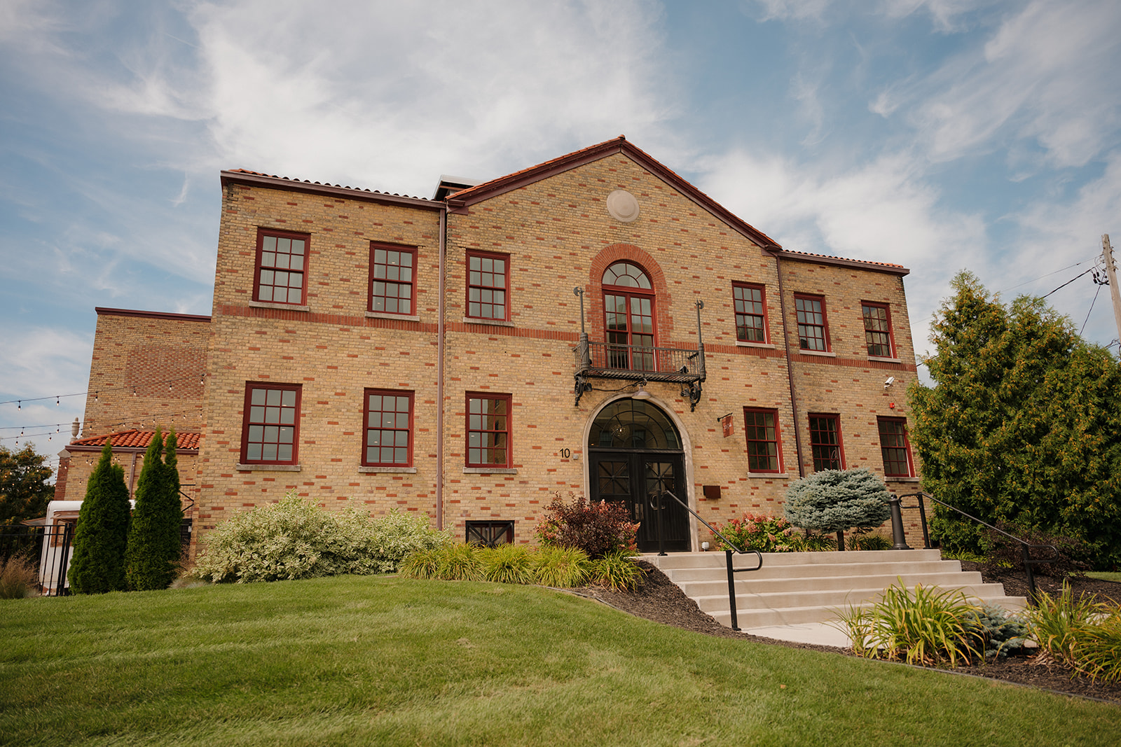 A wide view of the historic wedding venue with red-trimmed windows and manicured landscaping, perfect for couples seeking timeless charm in Wisconsin.