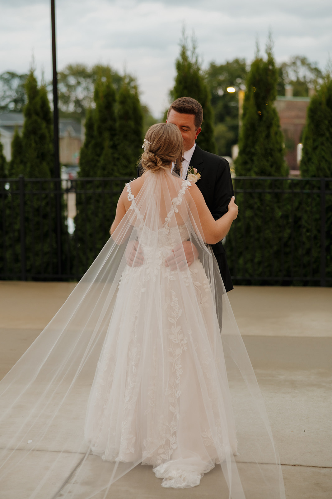 Facing one another in a quiet moment, the bride and groom gently hold hands—her veil softly trailing behind her.