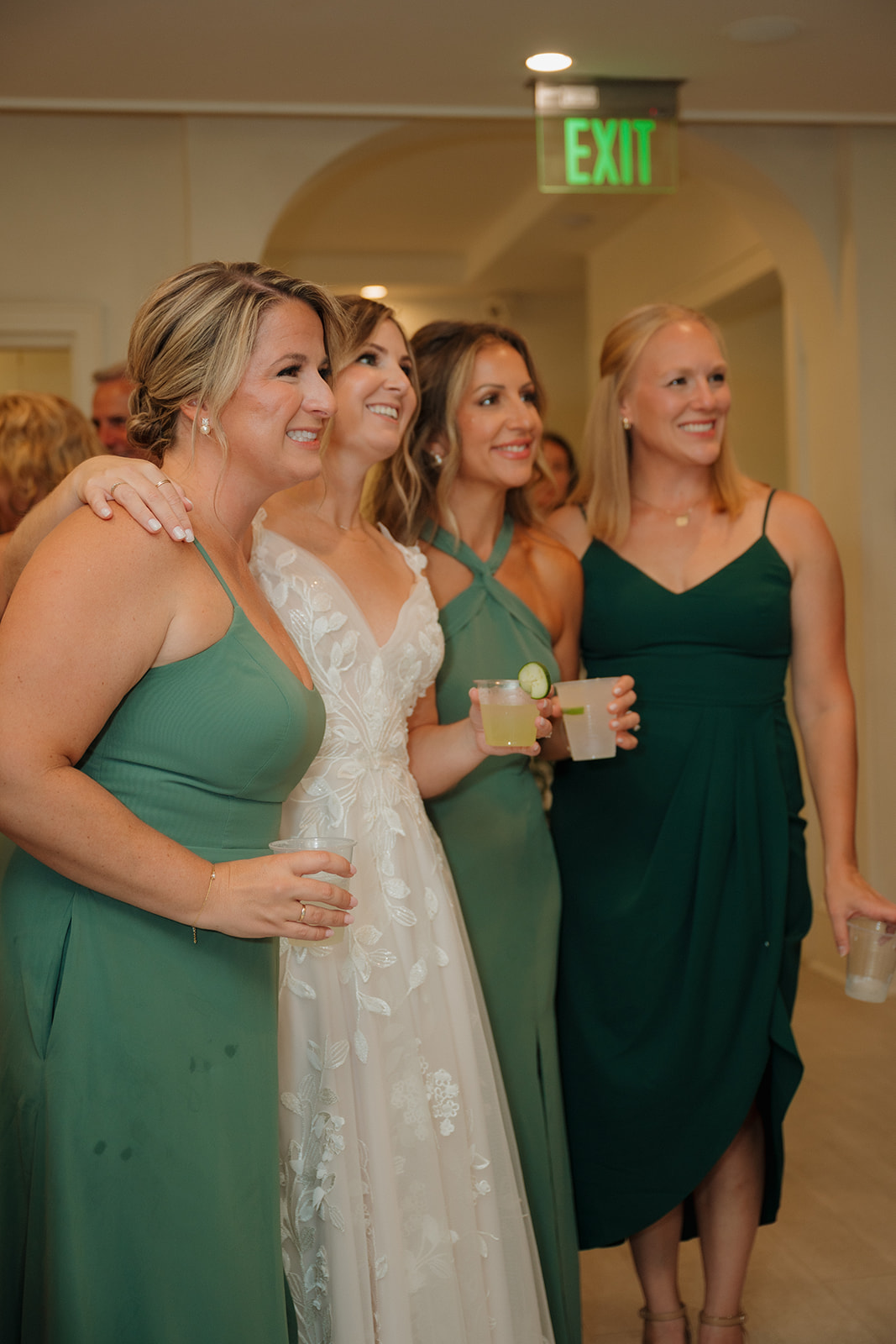 The bride and her bridesmaids smile for a quick photo inside the reception, drinks in hand and laughter in the air.