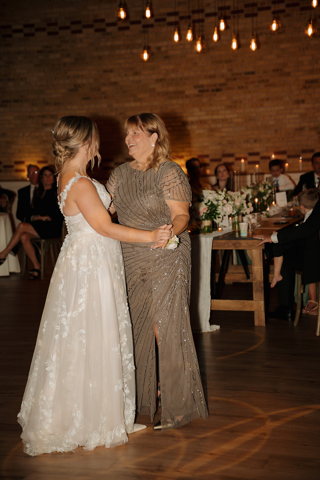 The bride dances with her mother under glowing Edison bulbs—one of those joyful moments wedding photographers in Wisconsin love to document.