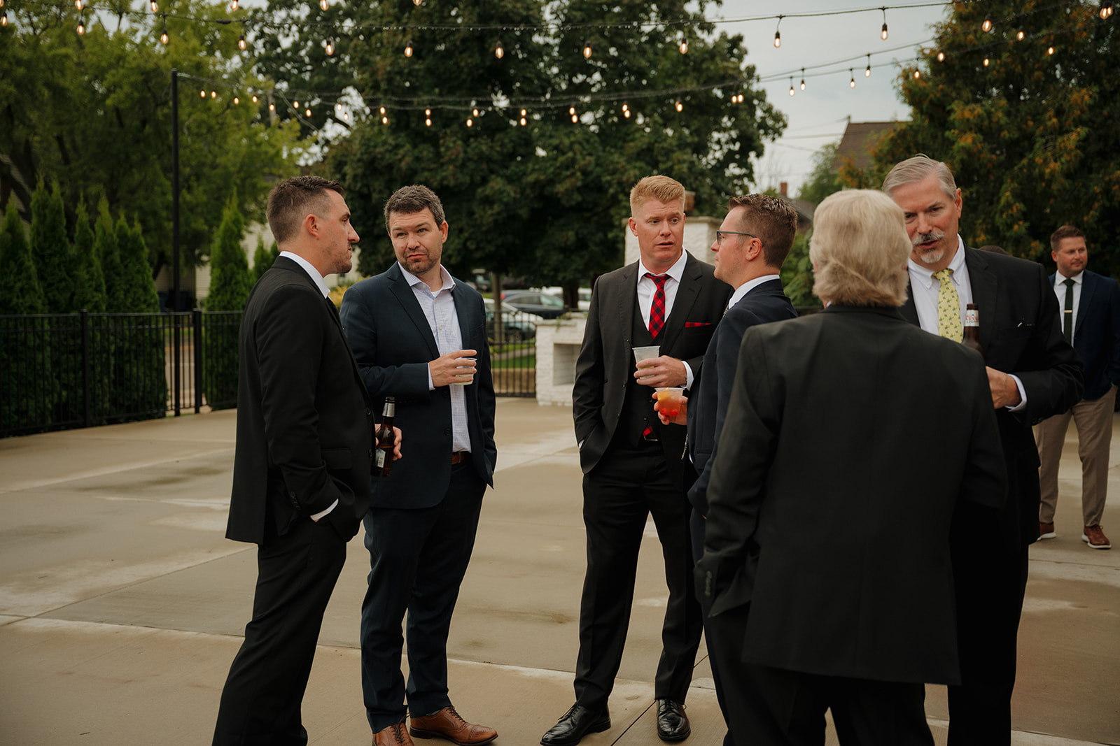 Groomsmen and guests mingle under string lights with drinks in hand, sharing laughs and stories as the celebration kicks off.