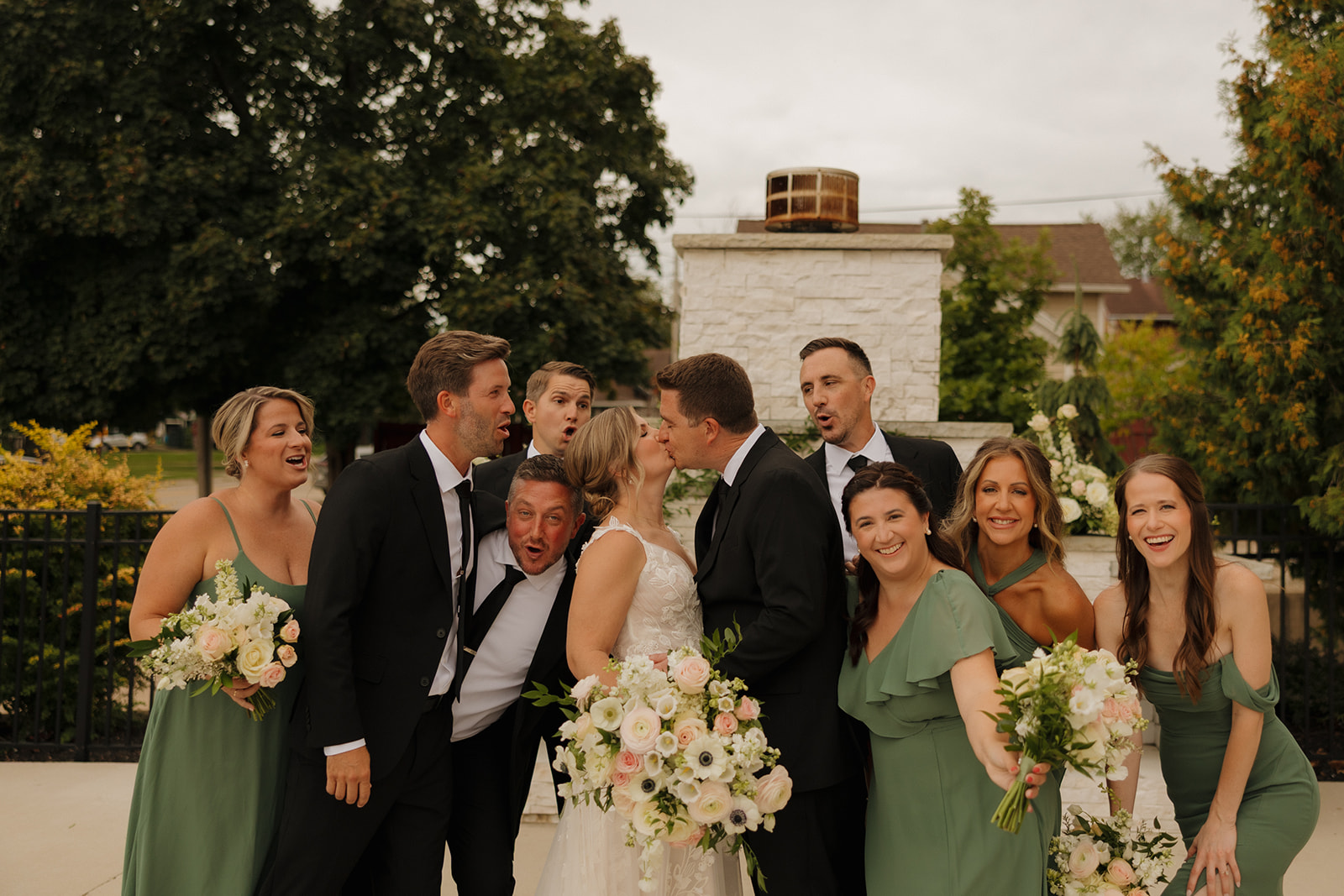 The couple shares a kiss while the entire wedding party cheers around them, bringing the fun and love in one epic group shot.