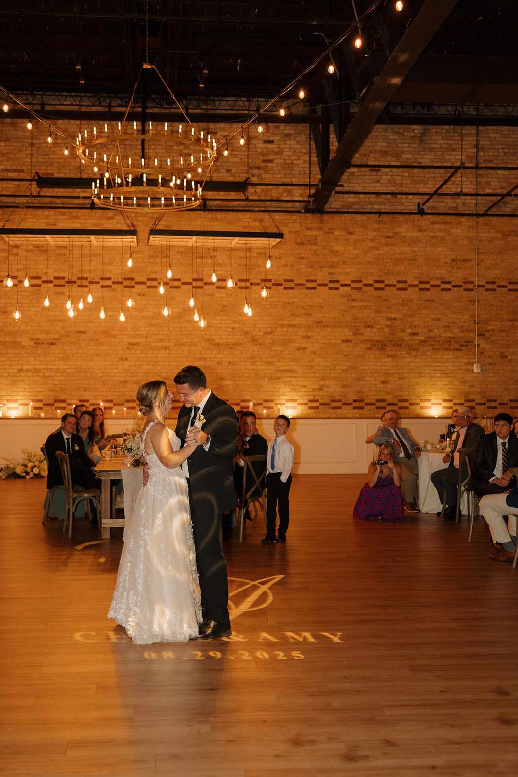 The couple’s first dance glows under chandeliers and warm lights, with their names and date projected on the floor—an iconic moment for wedding photographers in Wisconsin to document.