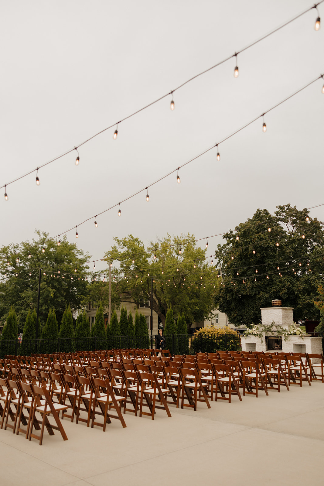 Rows of wooden chairs line the outdoor ceremony space under glowing string lights, ready to welcome guests for a beautiful celebration.