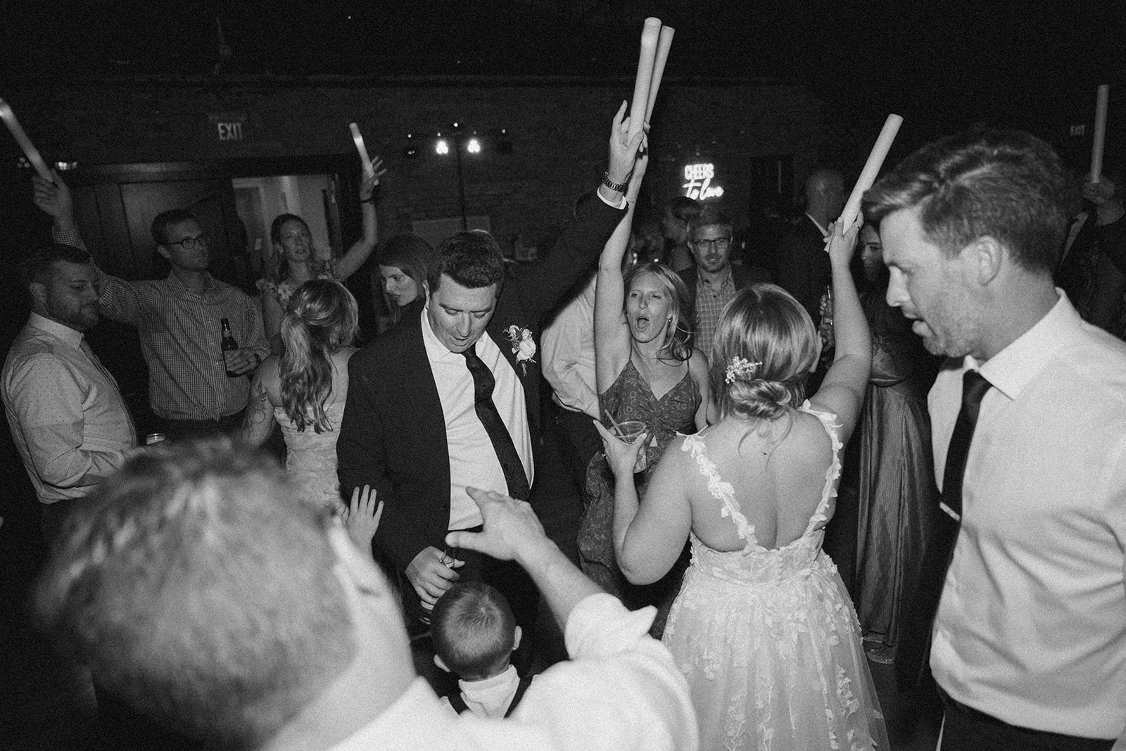 The couple dances in the middle of a packed floor, surrounded by friends raising glow sticks and singing along—a high-energy scene wedding photographers in Wisconsin never miss.