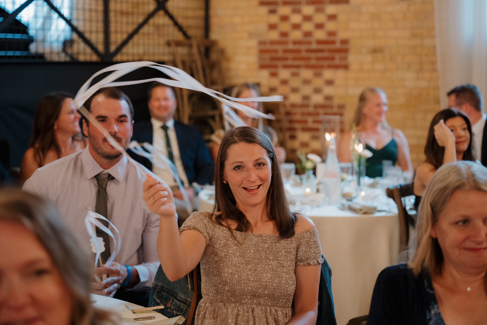 A guest joyfully waves a white ribbon wand during the reception, celebrating the newlyweds with a smile and playful spirit.
