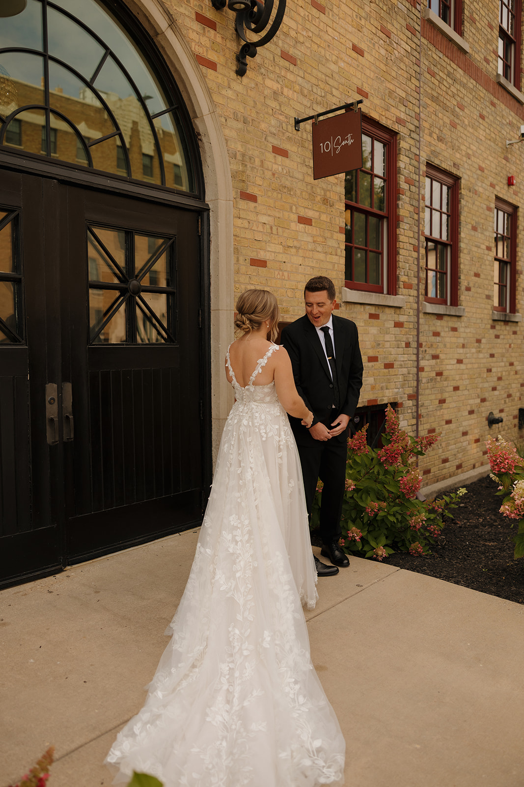 The couple locks eyes during their first look outside a brick building, surrounded by florals and soft golden light—captured by wedding photographers in Wisconsin.