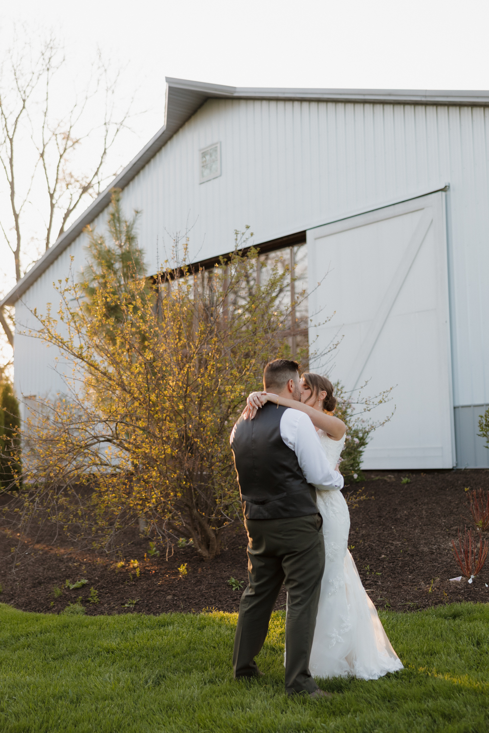 Bride and groom embracing at golden hour outside Boxed and Burlap Delavan with the white barn exterior glowing in soft light.