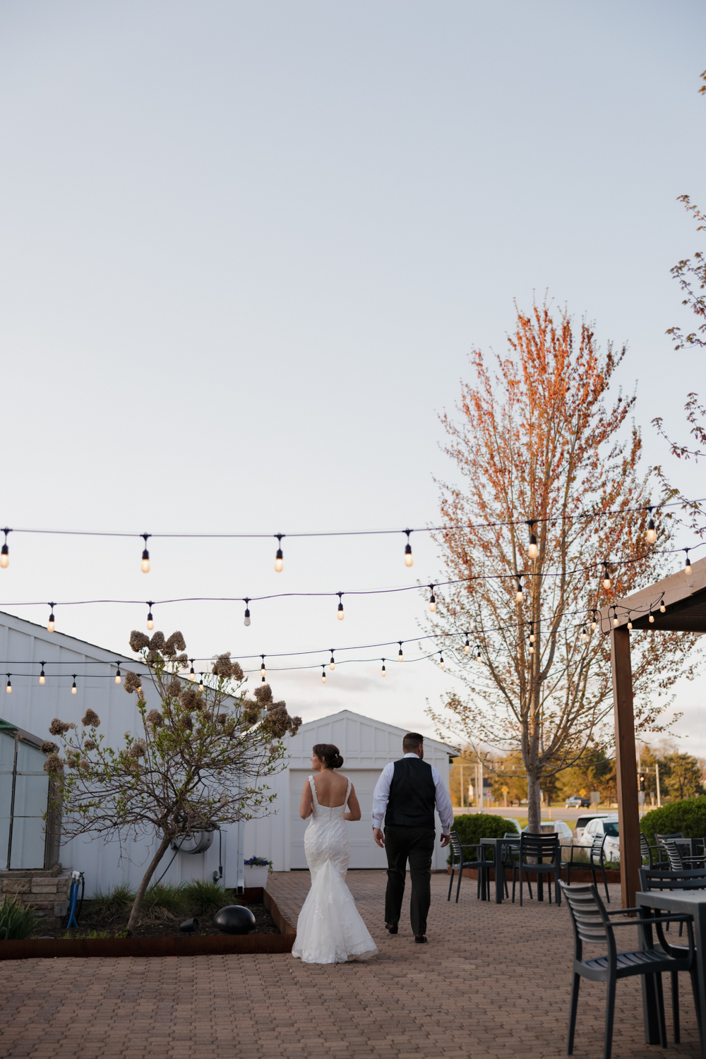 Bride and groom walking together at sunset outside Boxed and Burlap Delavan under café string lights and a glowing Wisconsin sky.