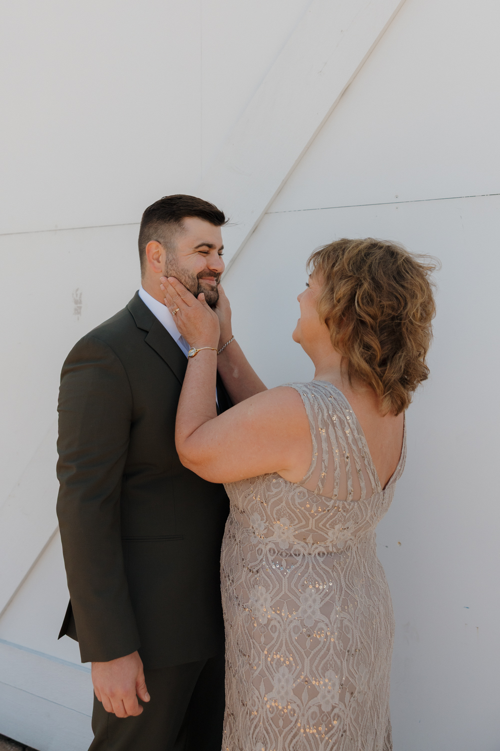 Mother gently holding the groom’s face and smiling at him outside Boxed and Burlap Delavan before the ceremony.