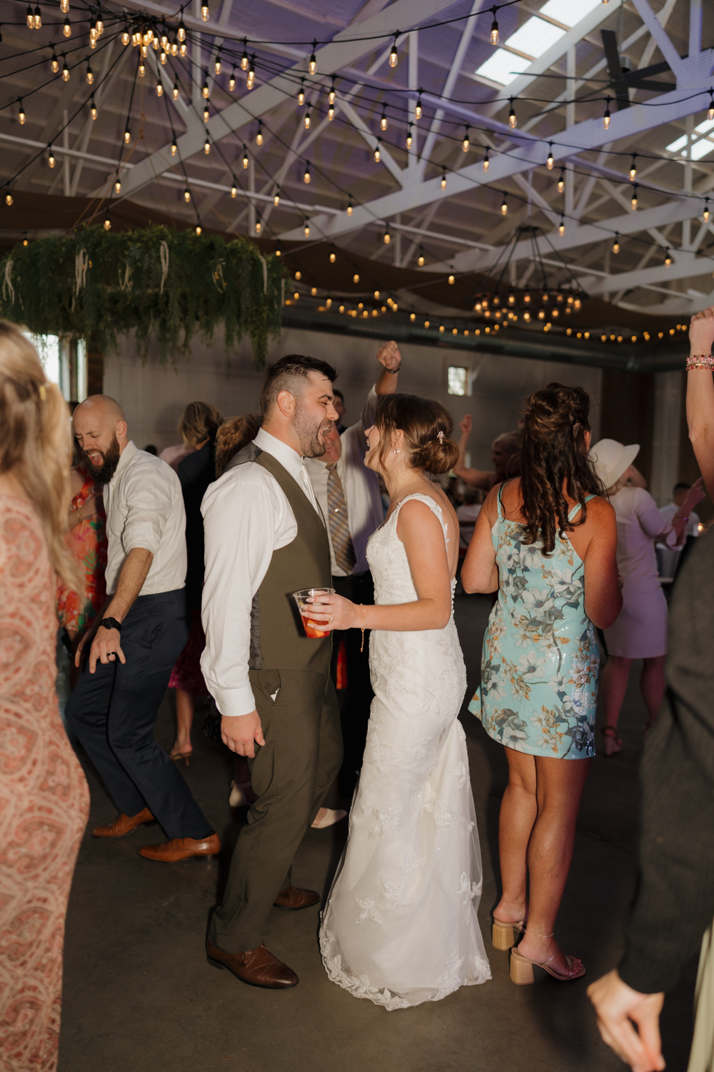 Bride and groom laughing together on the dance floor under string lights during their wedding reception.